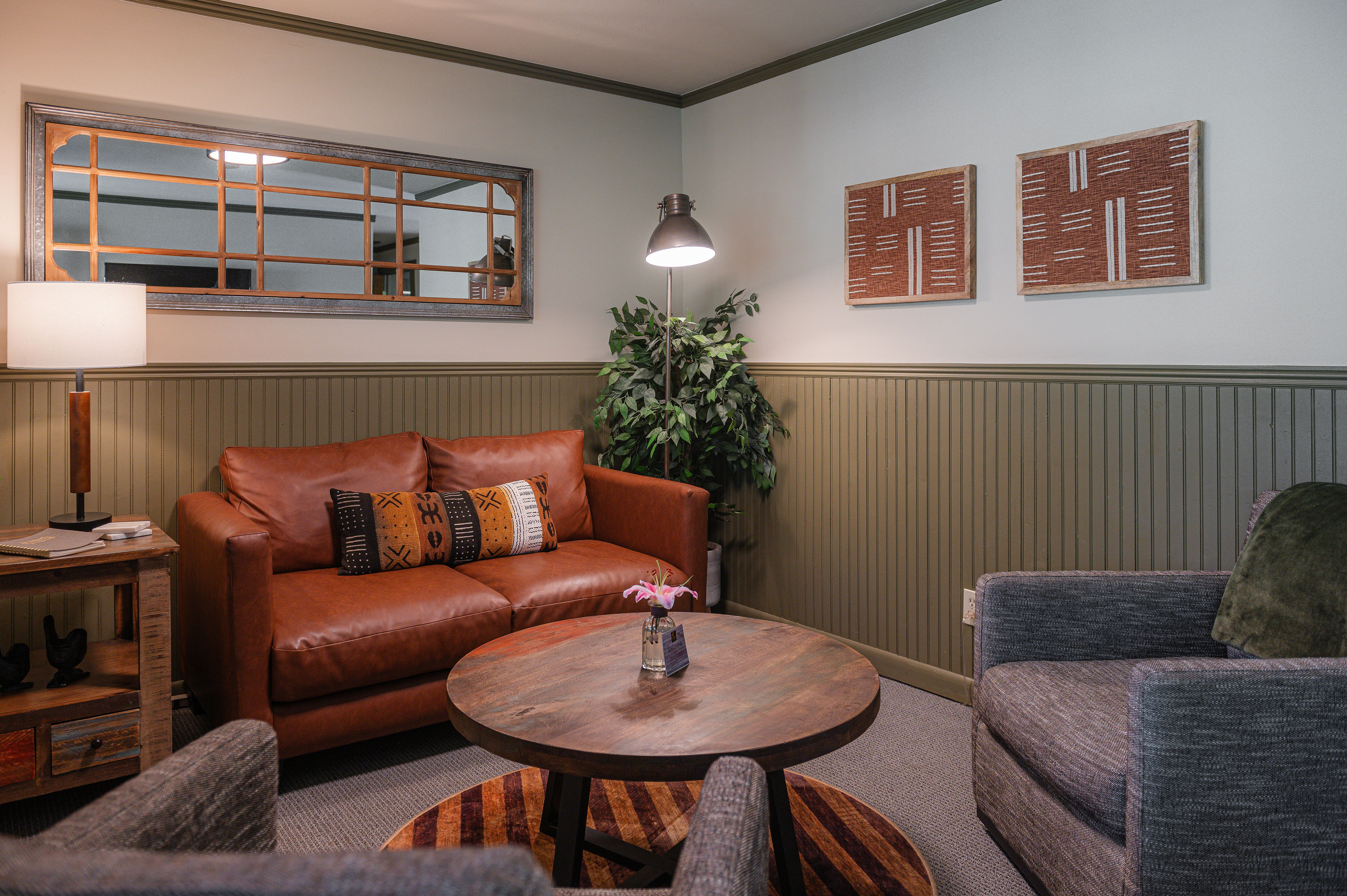 sitting room, brown leather love seat, and two gray chairs with round coffee table in middle.
