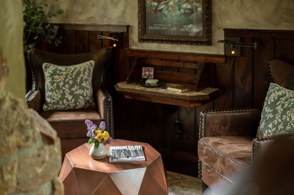 Sitting area with two brown deluxe chairs, an Atonement to rest your feet, and a gas fireplace. with log beams above.