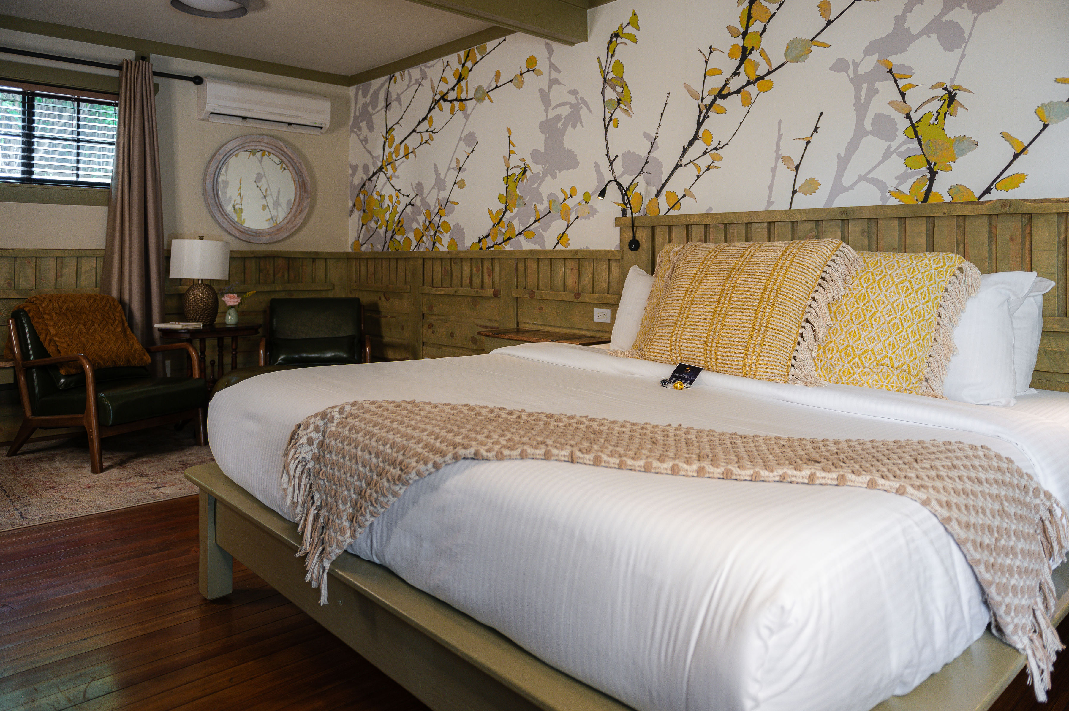 White bedding, green leather chairs, wood floors and graphic wall paper above the bed.