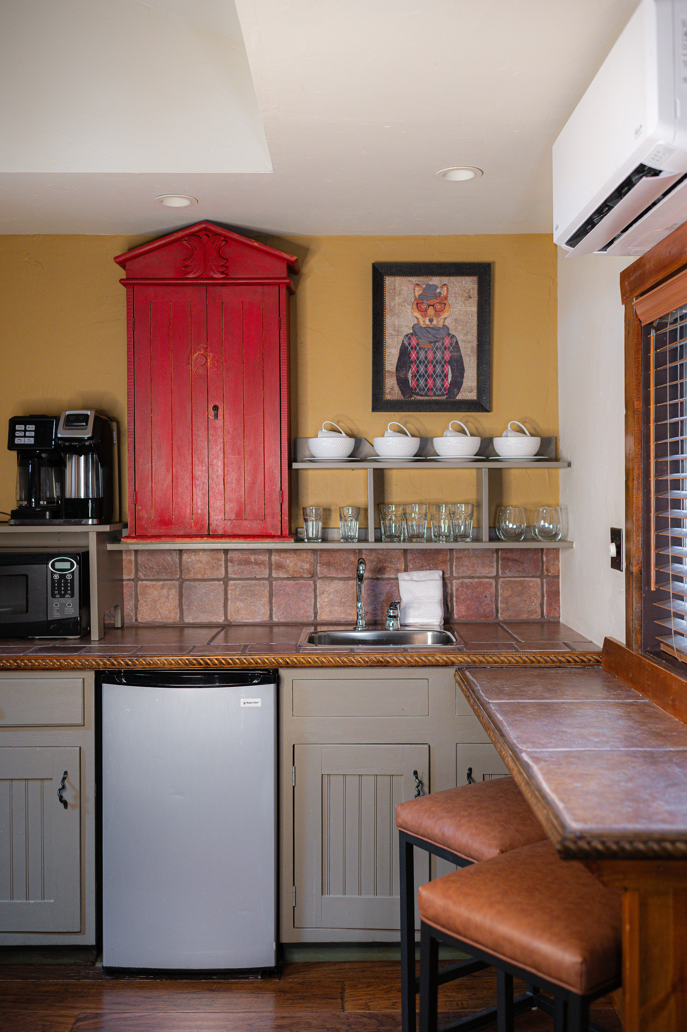 kitchenette with green cabinets below and open shelving with red cabinet above, microwave, mini-fridge, coffee maker and dishes