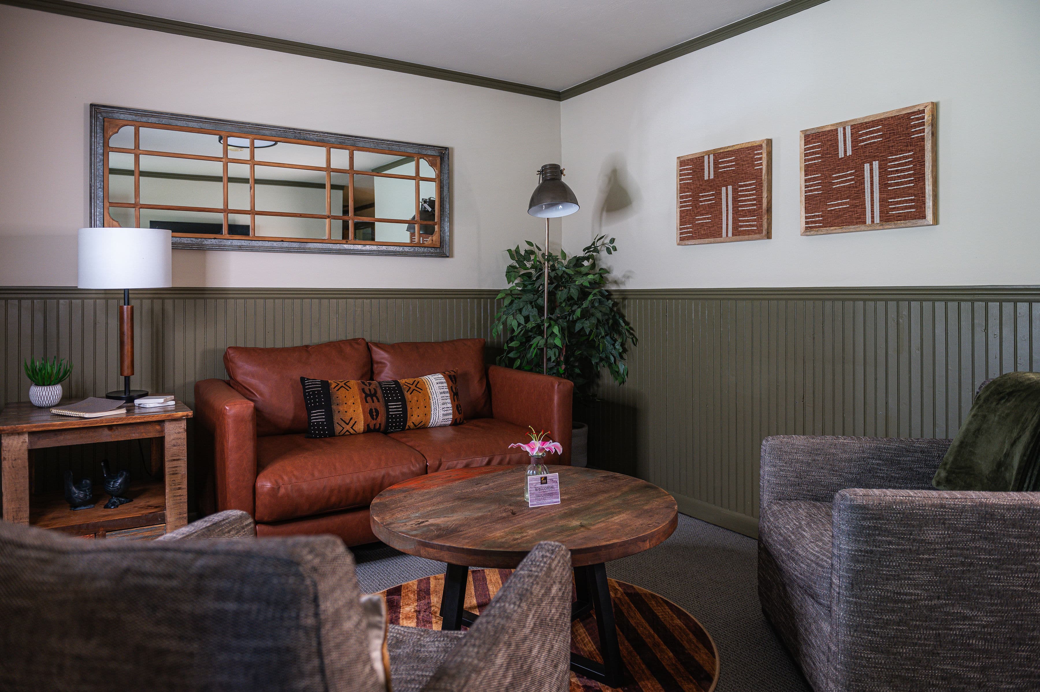 sitting room, brown leather love seat, and two gray chairs with round coffee table in middle.