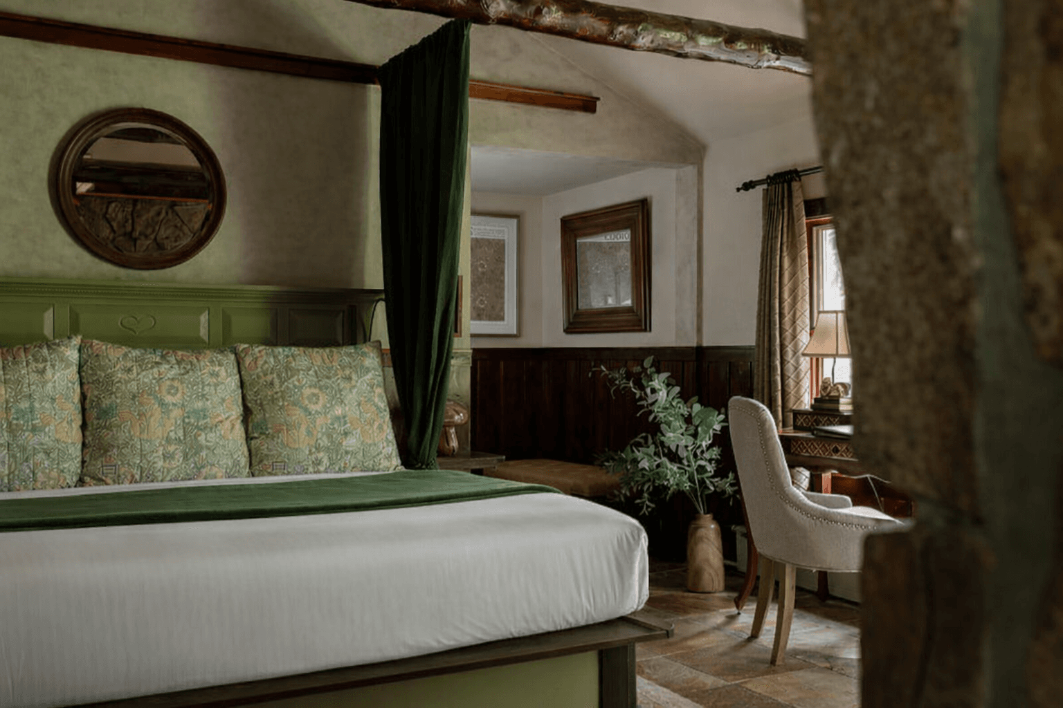King bed with soft brown throw, Aztec decorative pillows and log beams over the bed. moss rock Gas fireplace at foot of bed