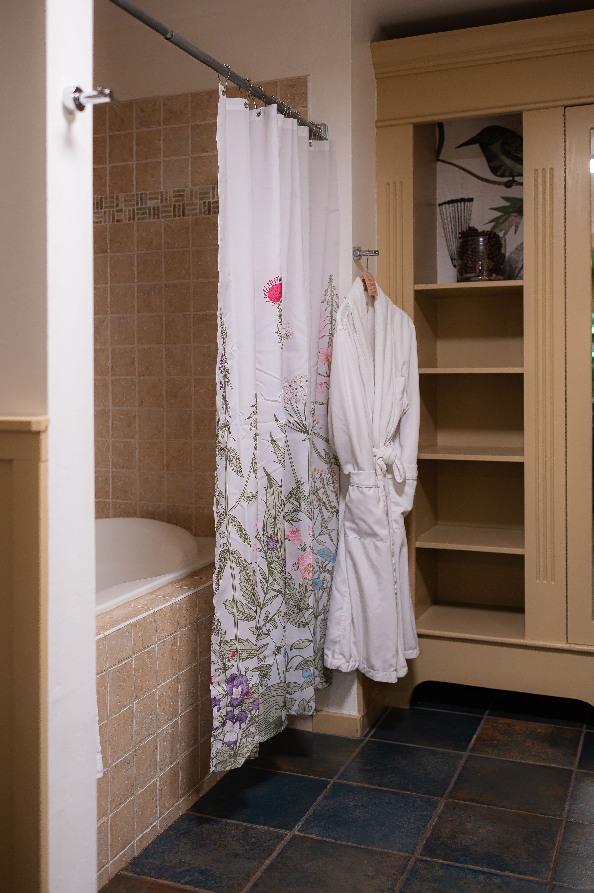 Jetted bathtub with tile surround, floral shower curtain and a white robe hanging up