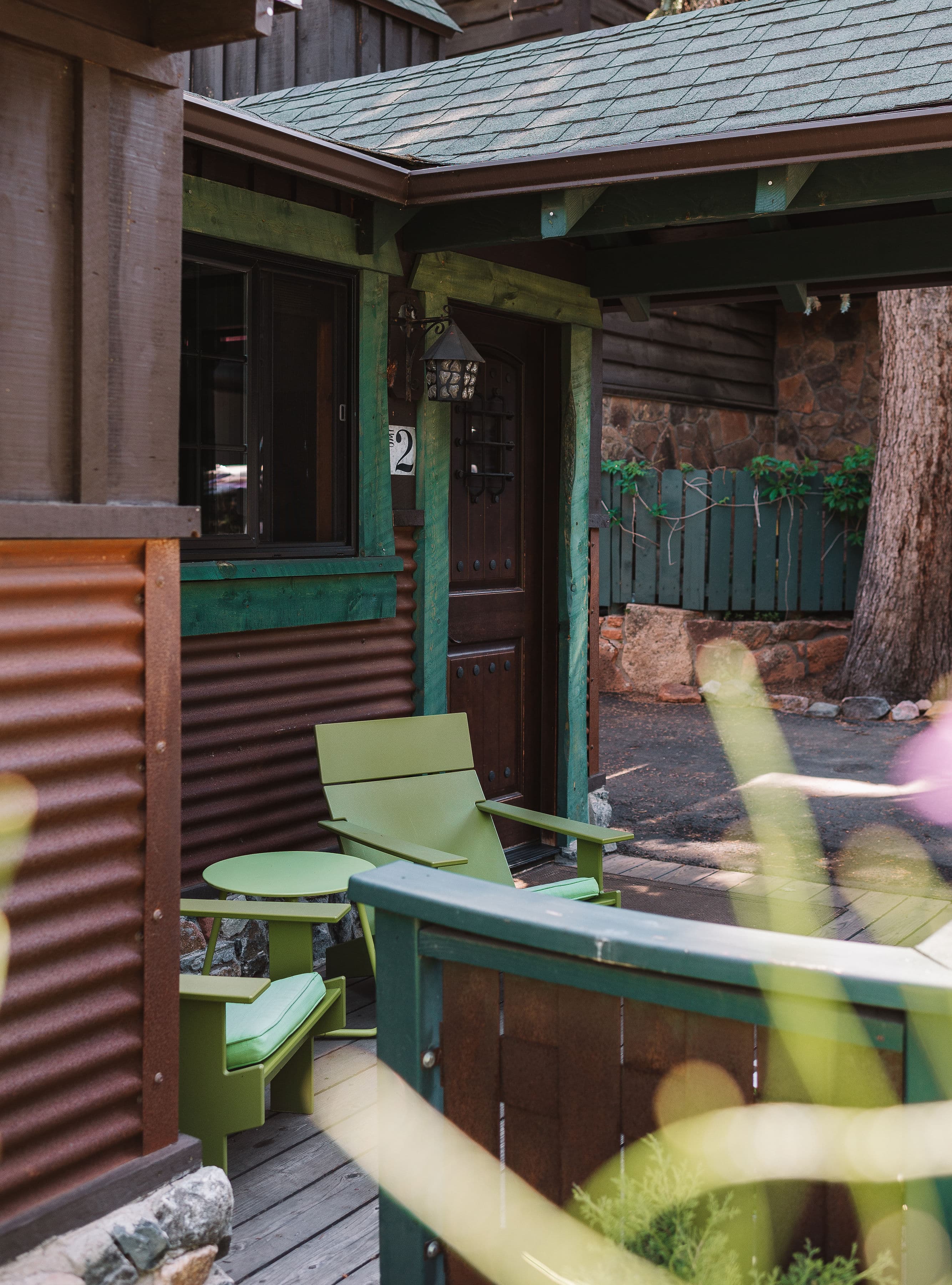 Patio on front side of cabin with two bright green Adirondak chairs and a small table