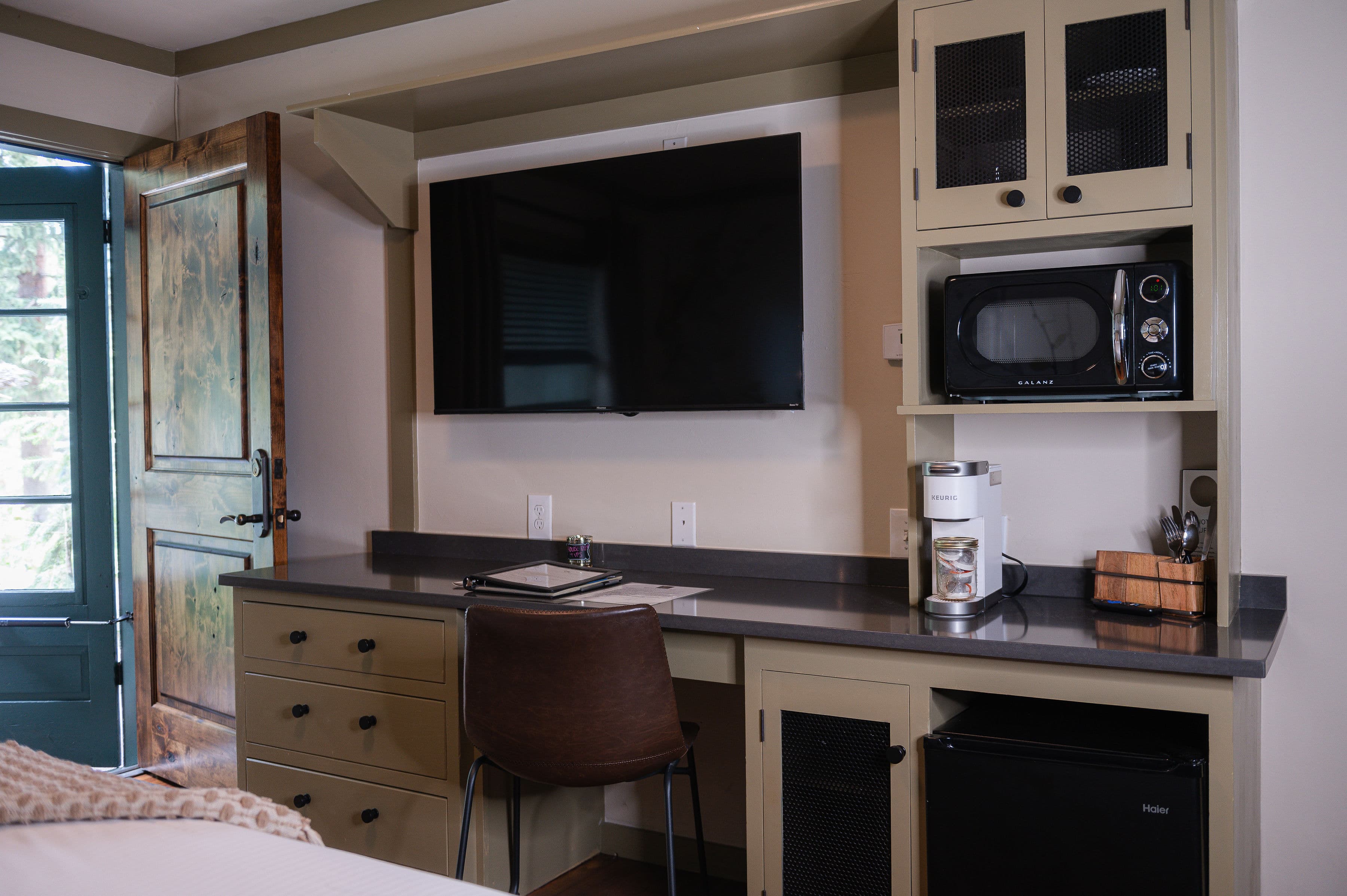 built in desk with stone top and cabinets, mounted flat screen smart tv, cube fridge, microwave and Keurig coffee maker.
