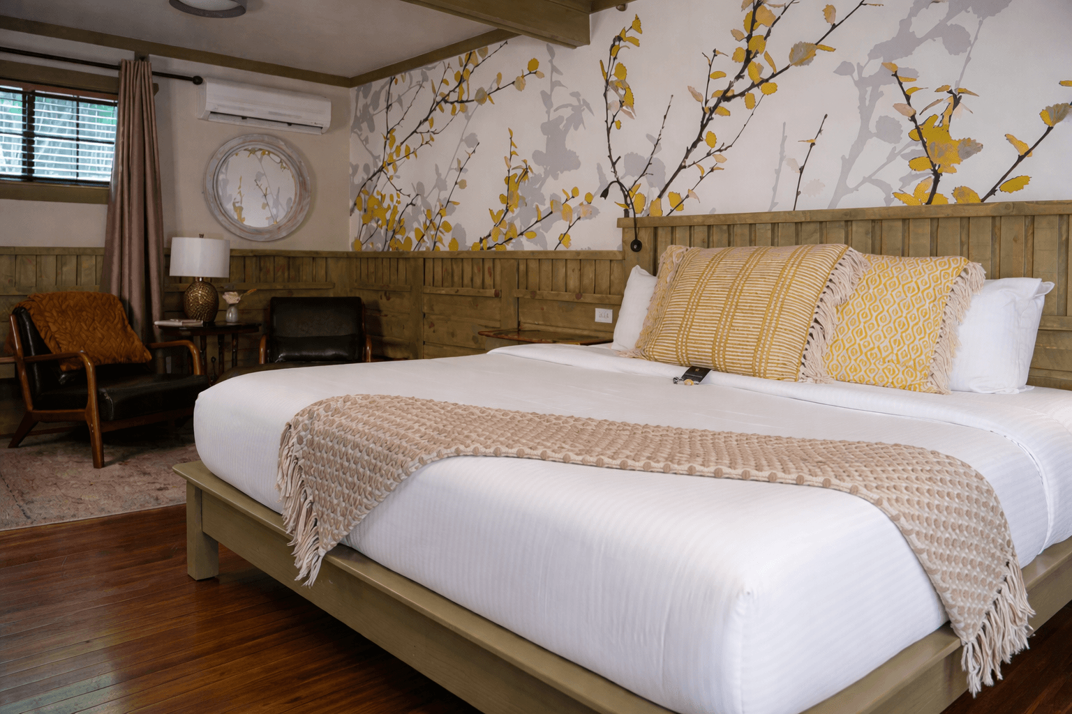 White bedding, green leather chairs, wood floors and graphic wall paper above the bed.