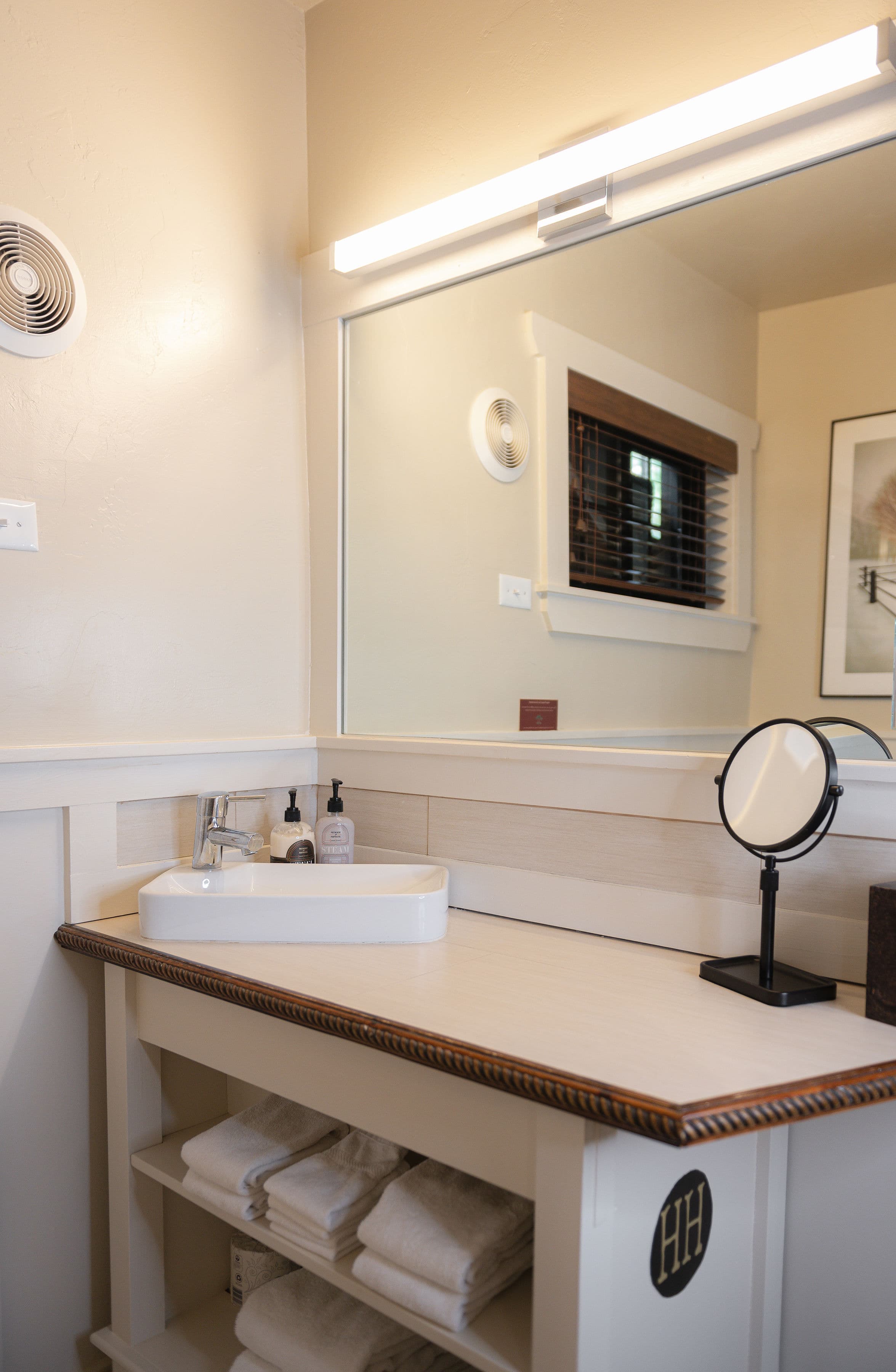 White bathroom vanity with shelves for towels below sink and large mirror.