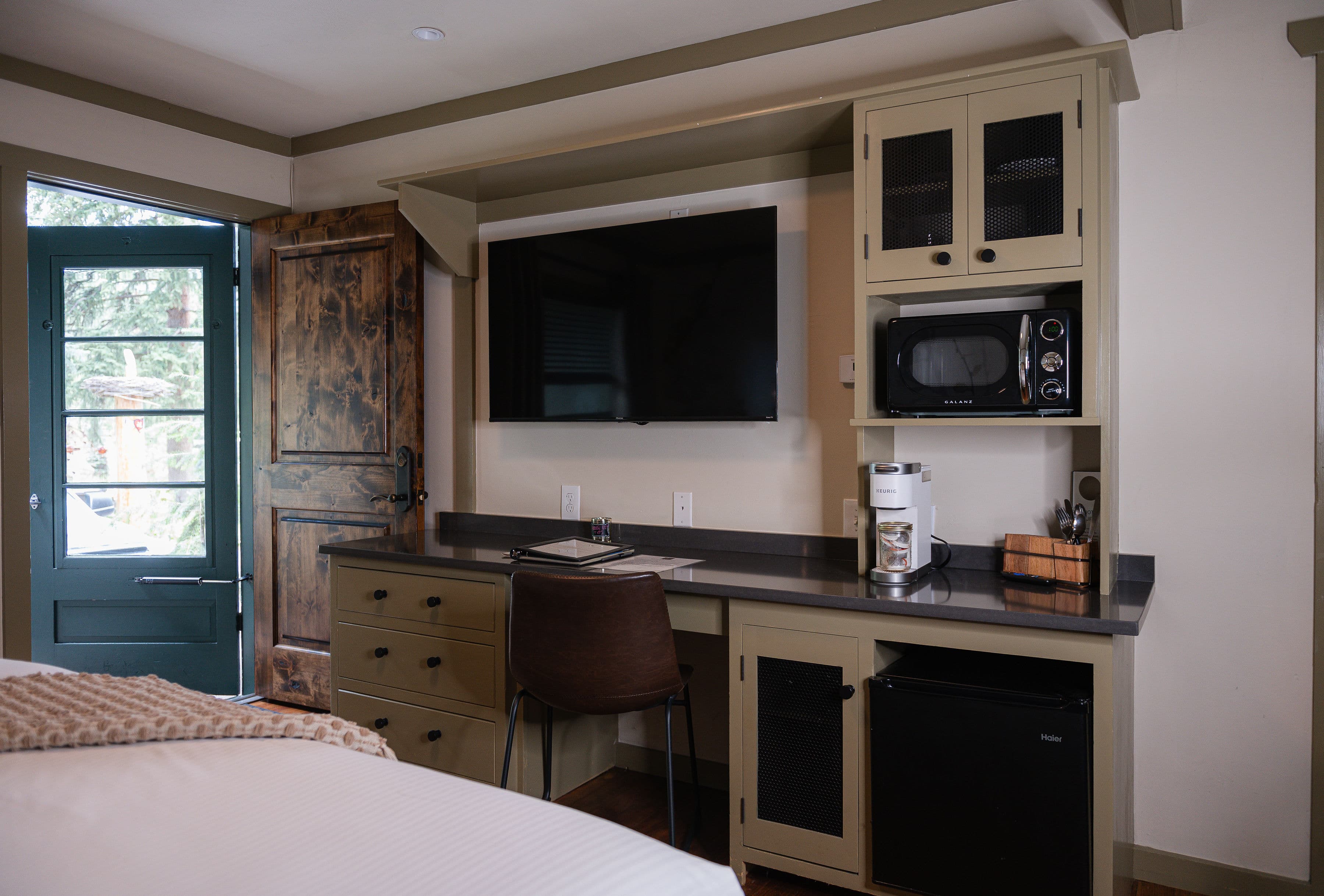 built in desk with cabinets and stone desk, mounted flat screen smart TV, cube fridge, microwave and keurig coffee maker