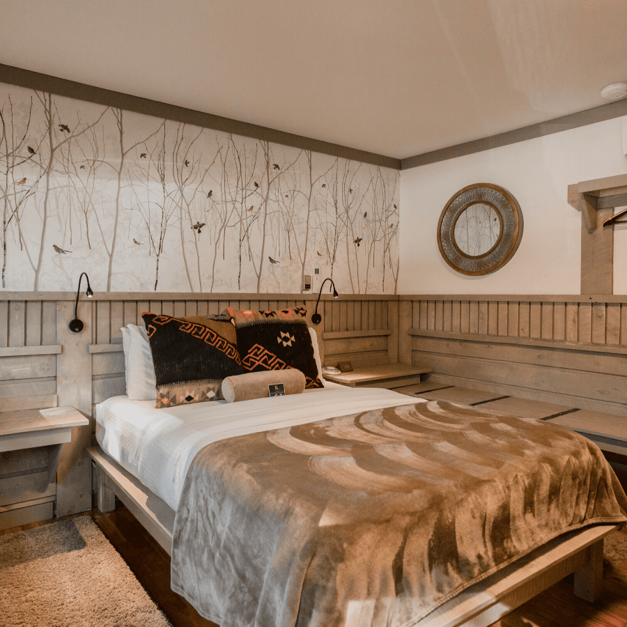 Queen memory foam platform bed with velveteen blanket and textured pillows, light green wainscotting and decorative bird wallpaper above bed, luggage bench and hangers next to bed along wall.