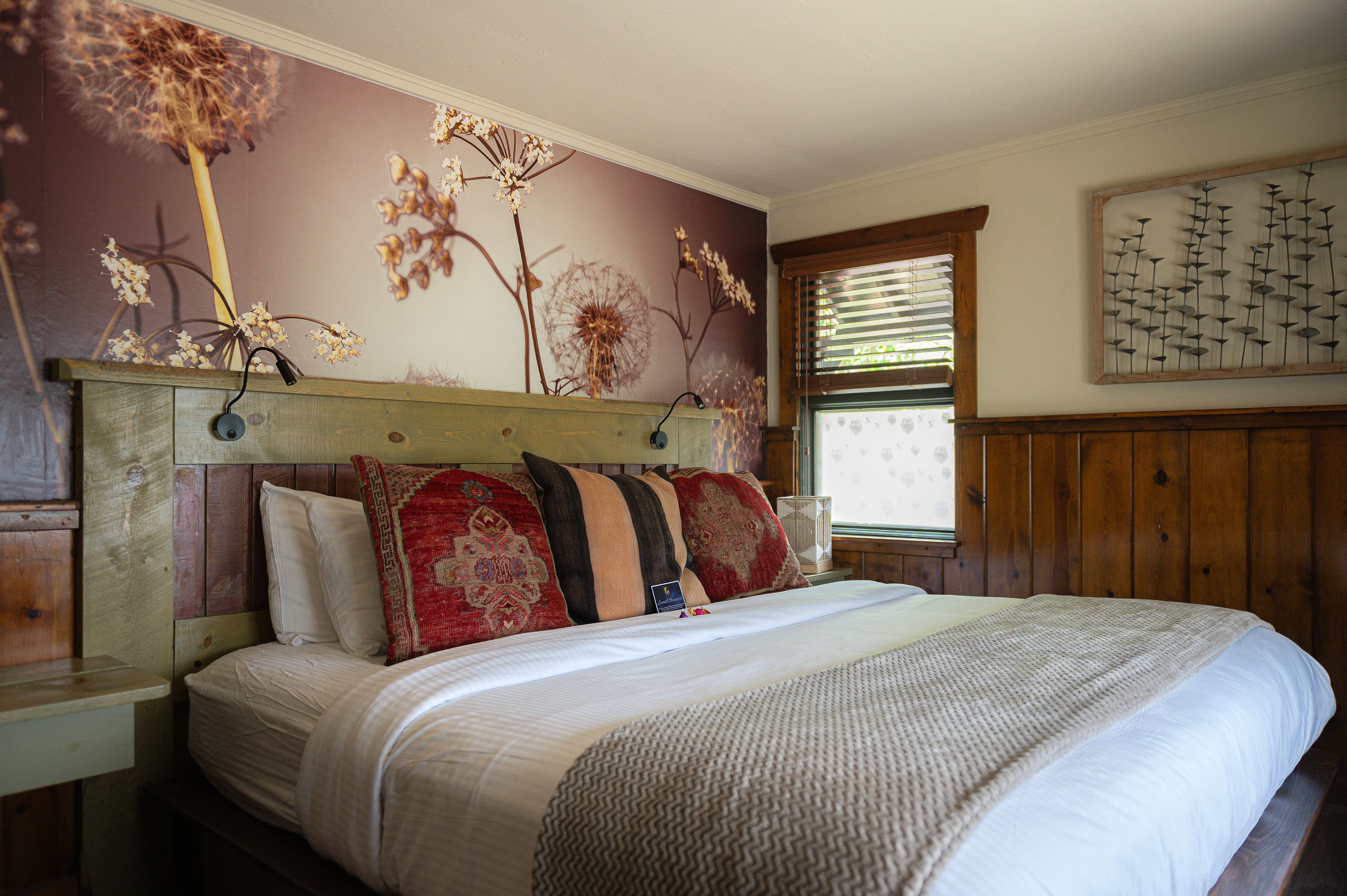 king bed with soft bedding, graphic dandelion wallpaper above bed and wood paneling