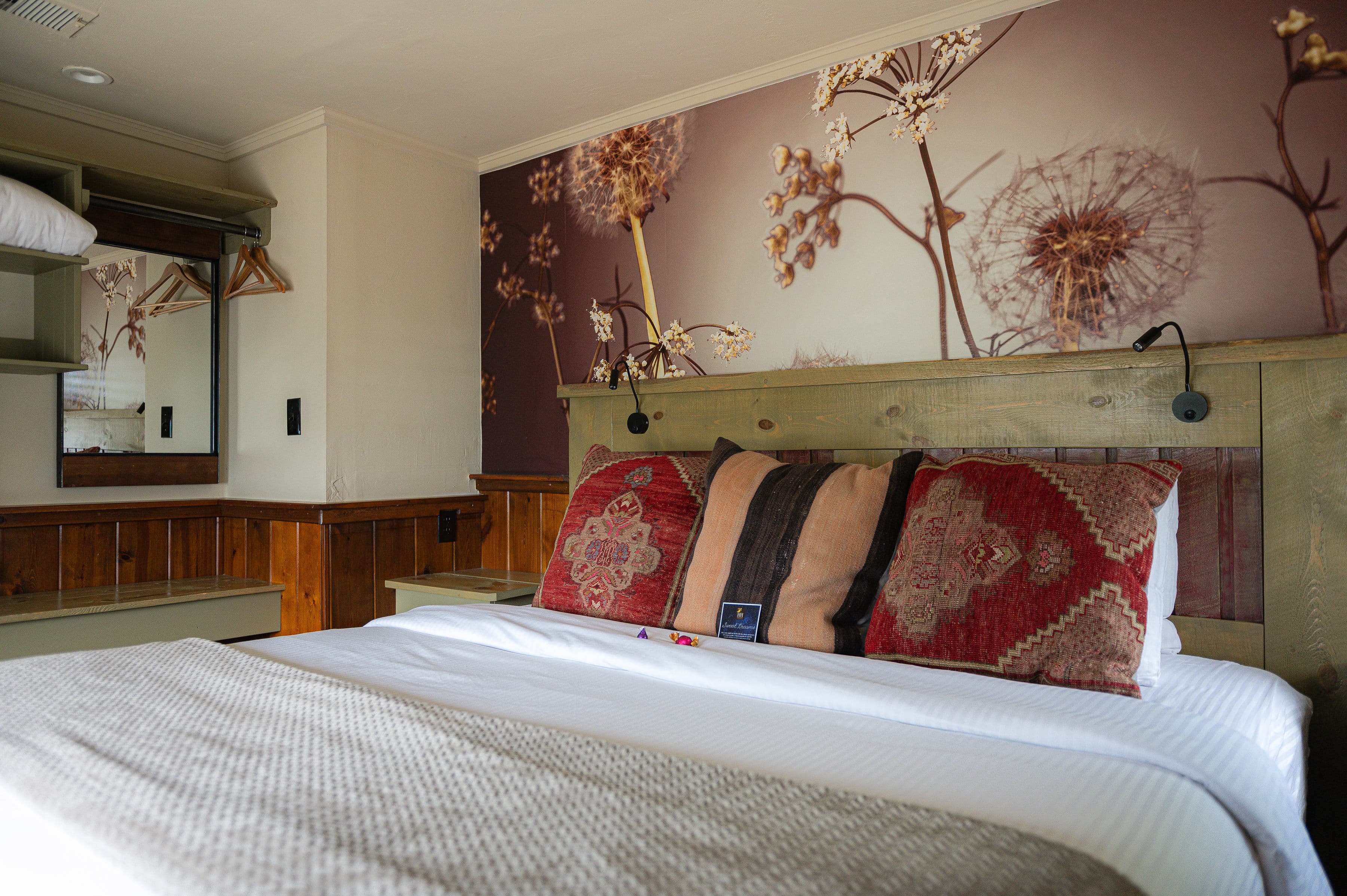 king bed with soft bedding, graphic dandelion wallpaper above bed and wood paneling