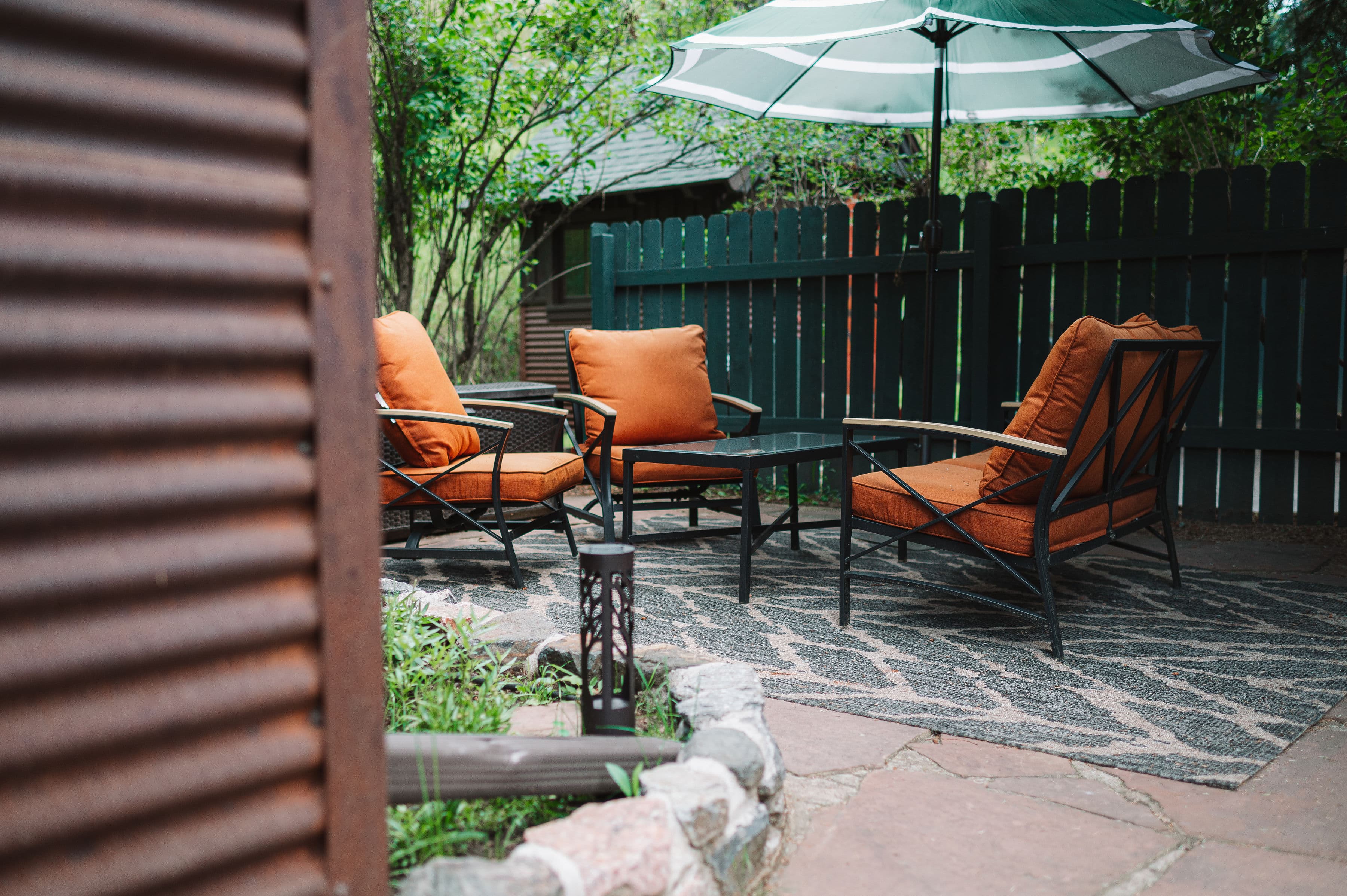 private patio with love seat and two chairs with orange cushions, coffee table and green striped umbrella