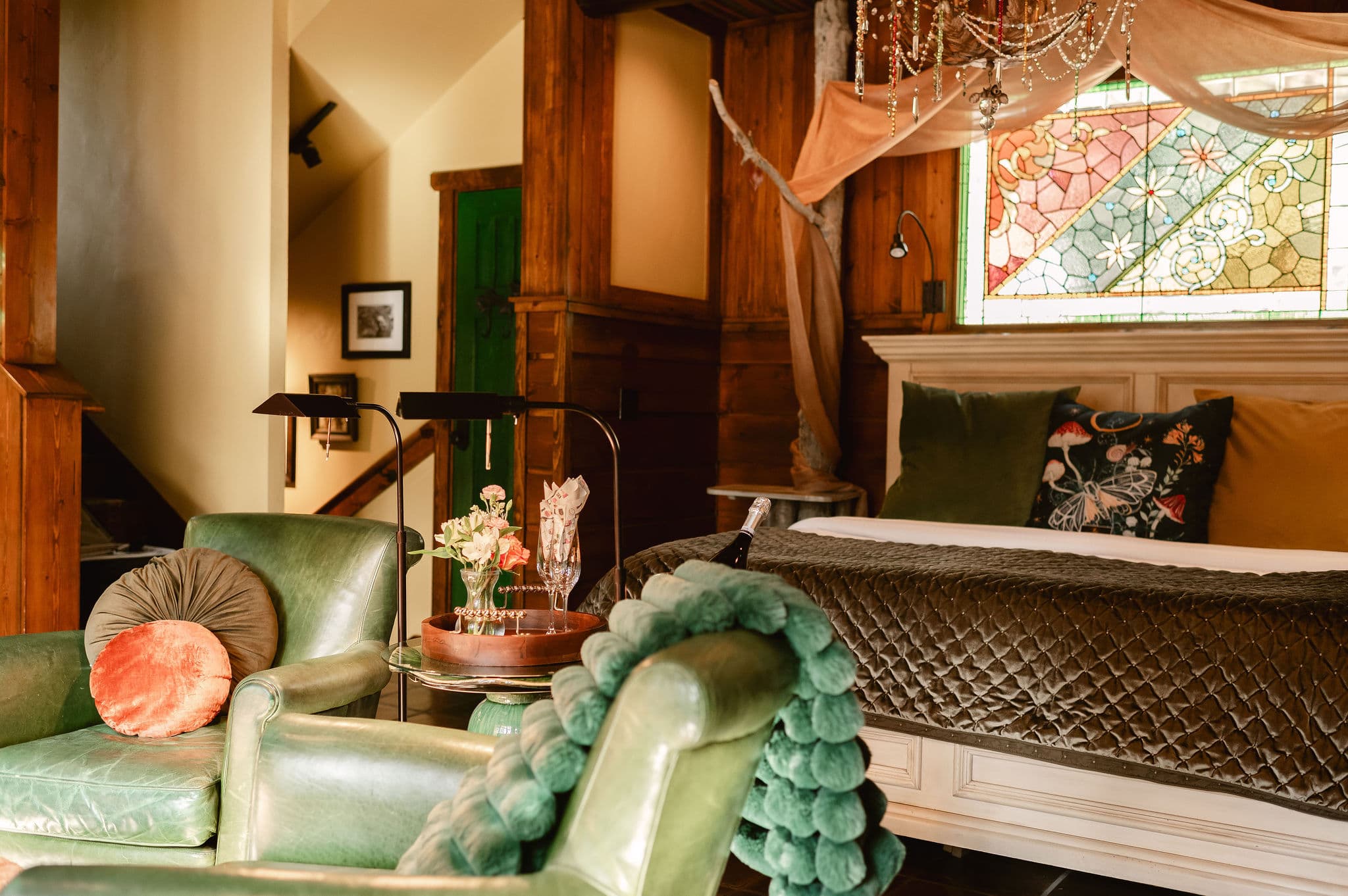 Brown tile floor, green leather chairs, colorful chandelier, fireplace, wood panel ceiling