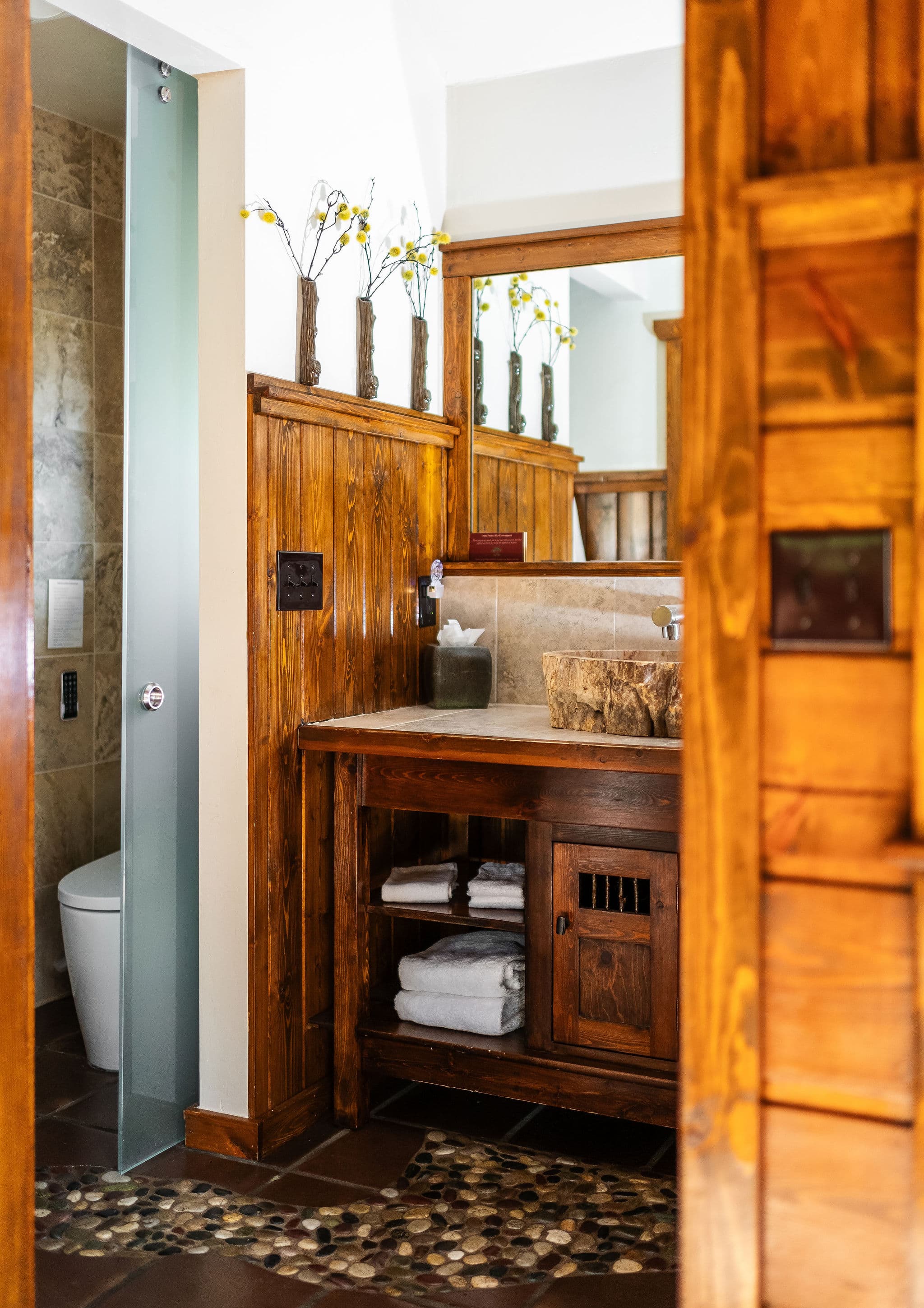 teak wood sink, pebbled floor of shower, big mirror and wood shelf