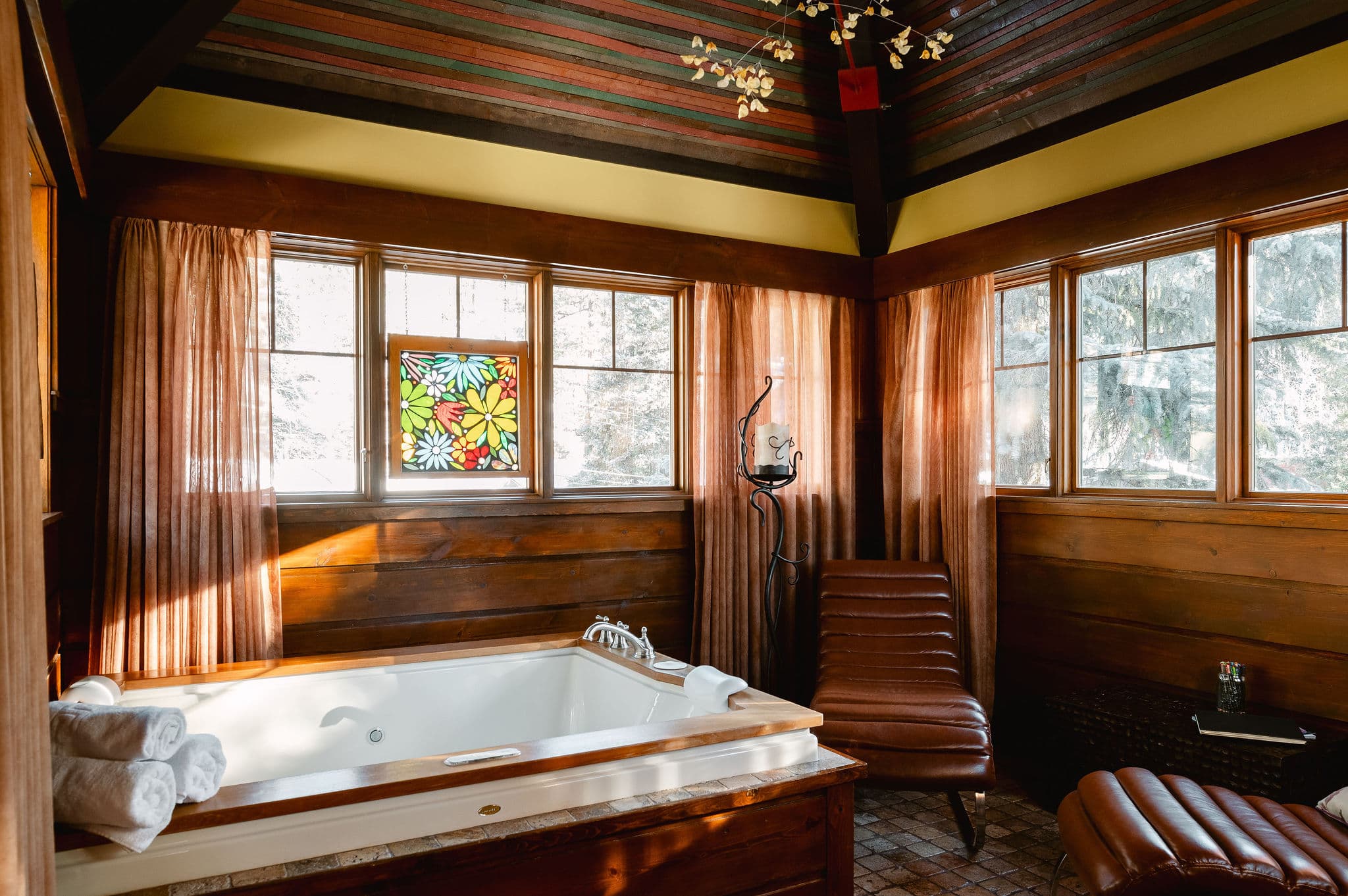 big tubw ith padded neck rests, mulit colored wood ceiling, stained glass in window and lounge chairs