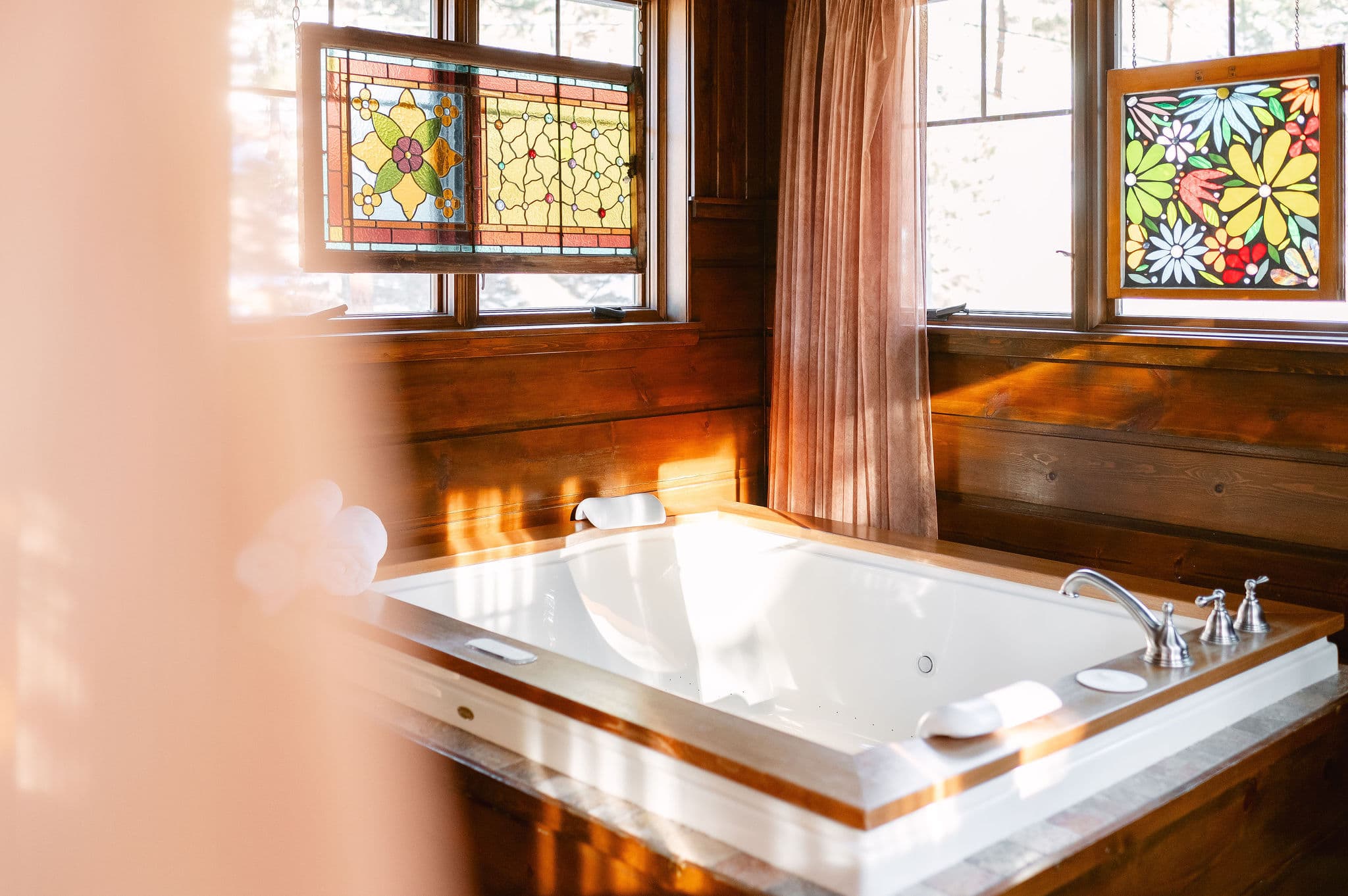 big tubw ith padded neck rests, mulit colored wood ceiling, stained glass in window