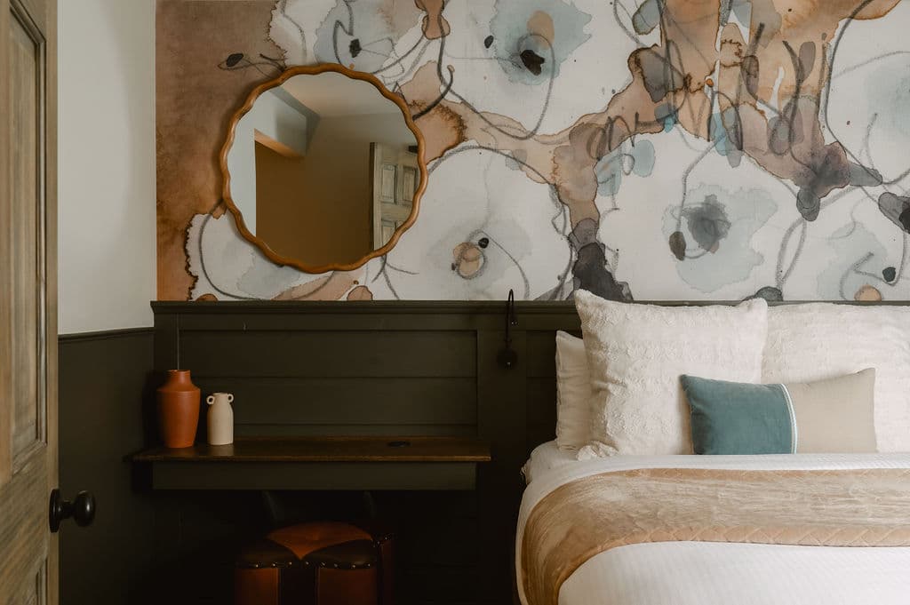 Queen bed with faux fur blanket and accent pillows. Green wainscotting and graphic wallpaper on walls.