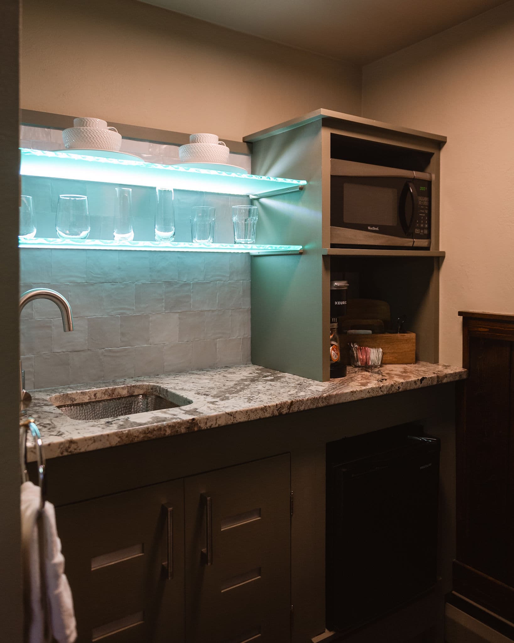 Kitchenette with green cabinetry, microwave, and a desk with mirror above