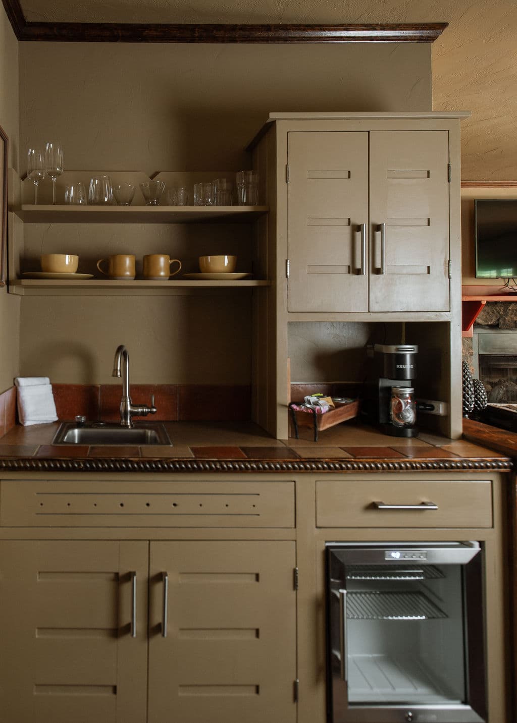kitchenette with bar sink, microwave, mini-fridge, keurig coffee maker, and shelves with dishes.