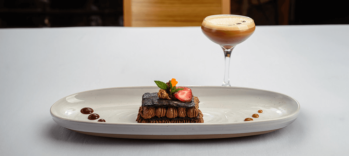 A decadent chocolate dessert garnished with a strawberry and mint, accompanied by a stylish cocktail.