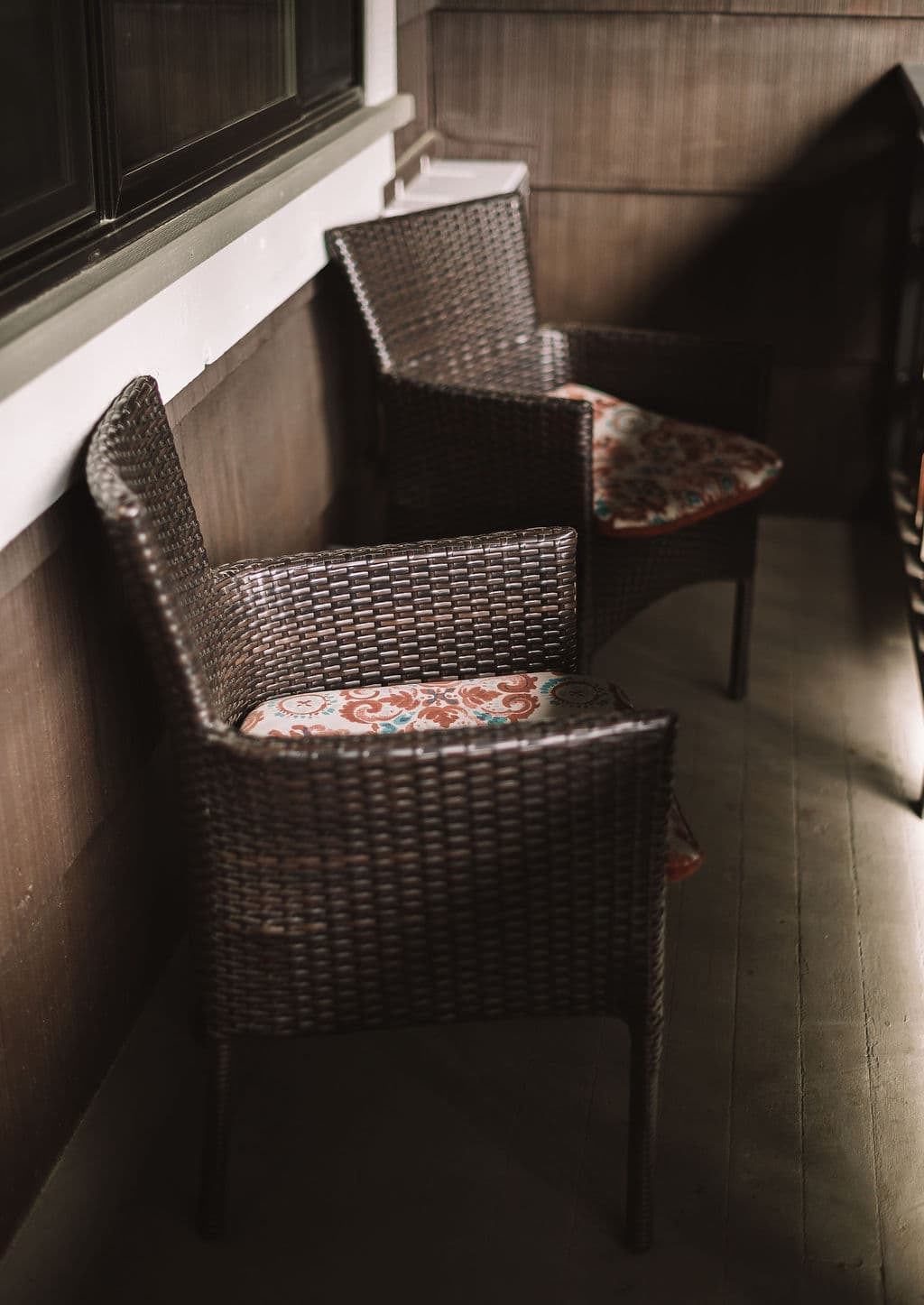 Two woven chairs with patterned cushions are positioned in a dimly lit corner.