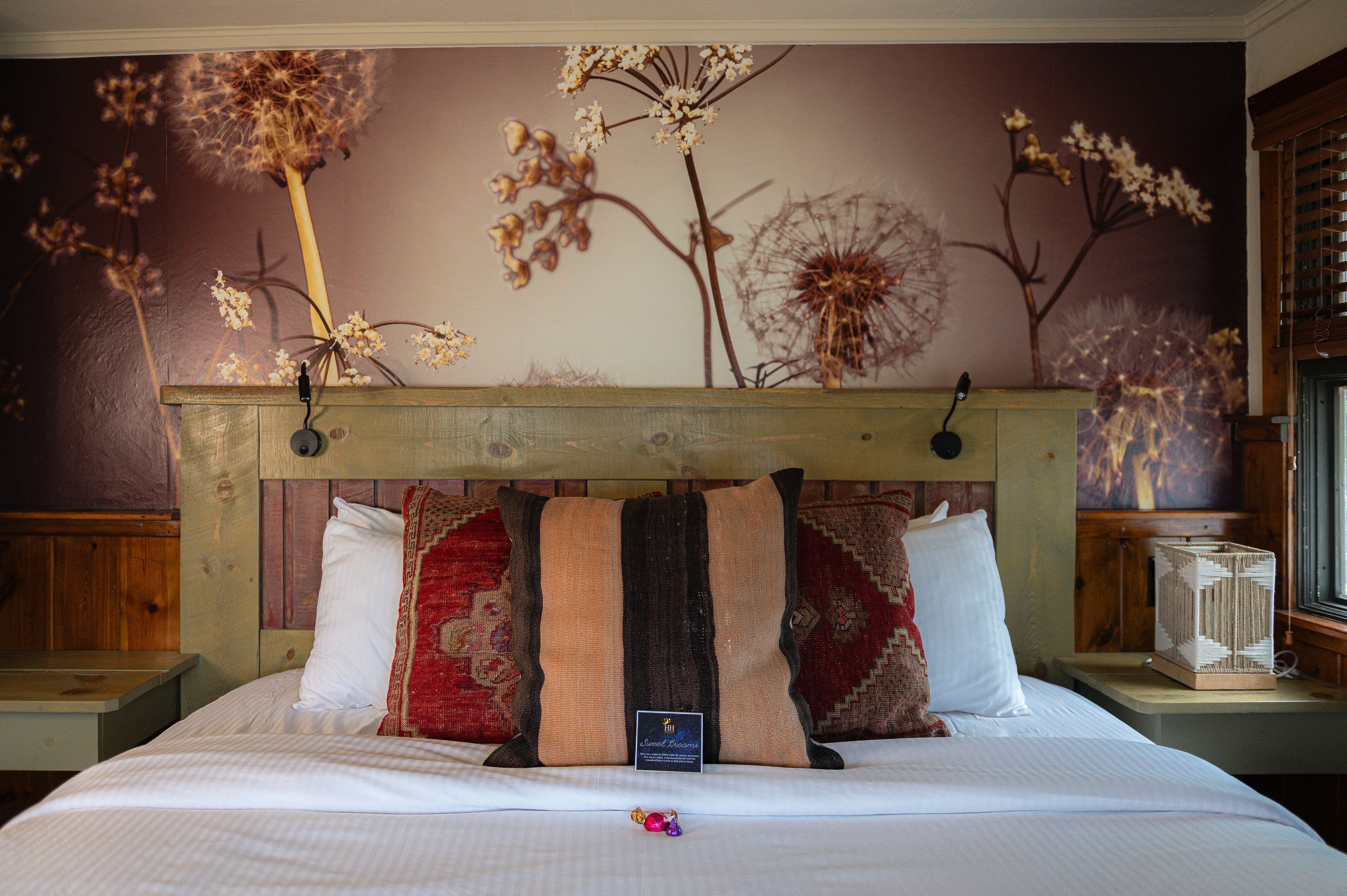 A cozy bedroom featuring a wooden headboard, decorative pillows, and a floral wallpaper backdrop.