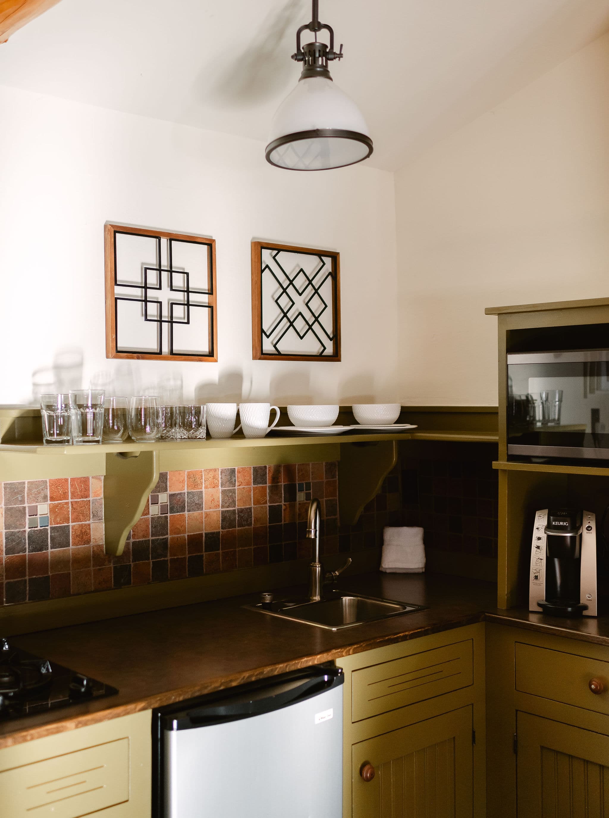 A cozy kitchen featuring a green color scheme, decorative wall art, glassware, and modern appliances.