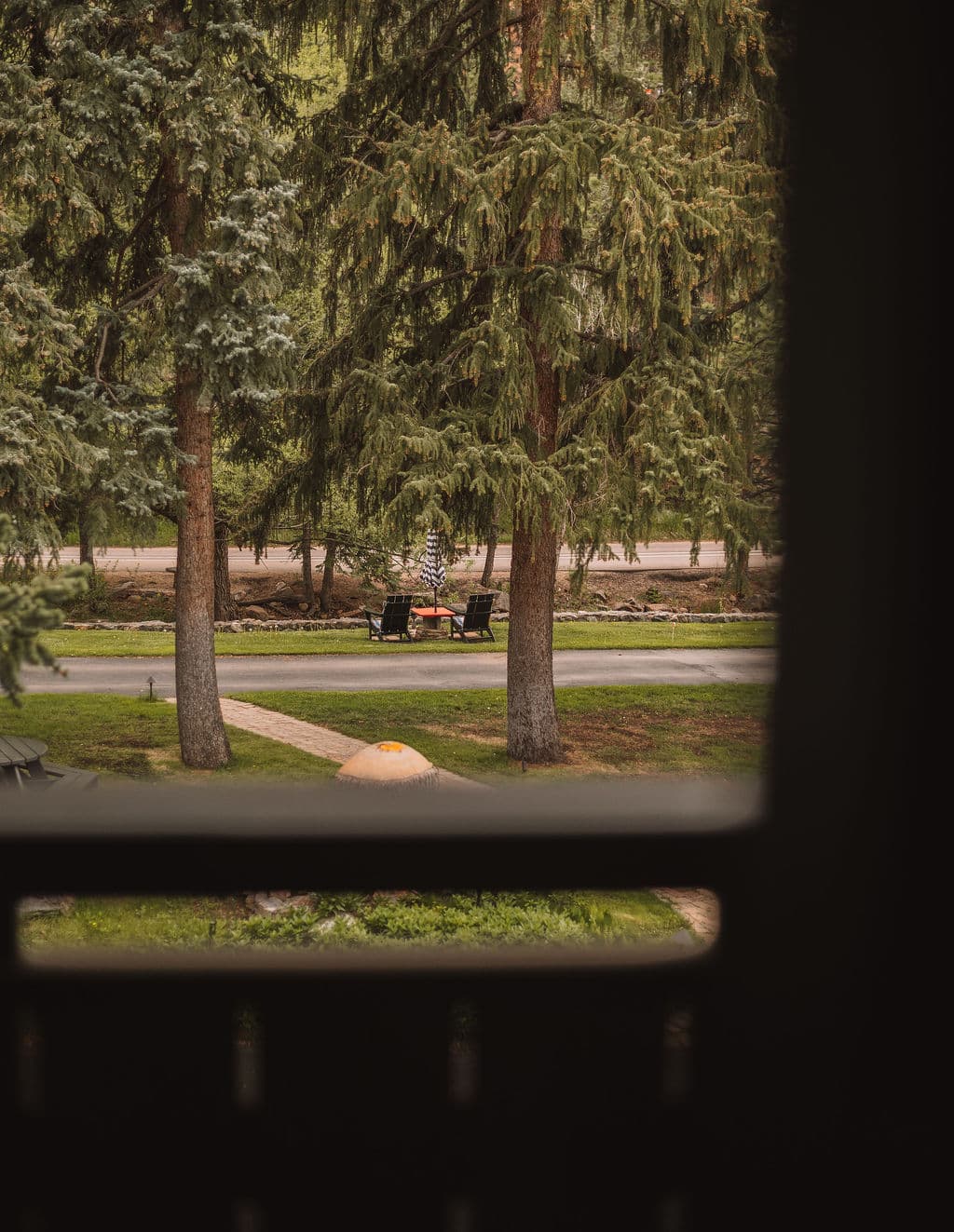 View through a window showcasing a serene scene of trees, a pathway, and outdoor seating.