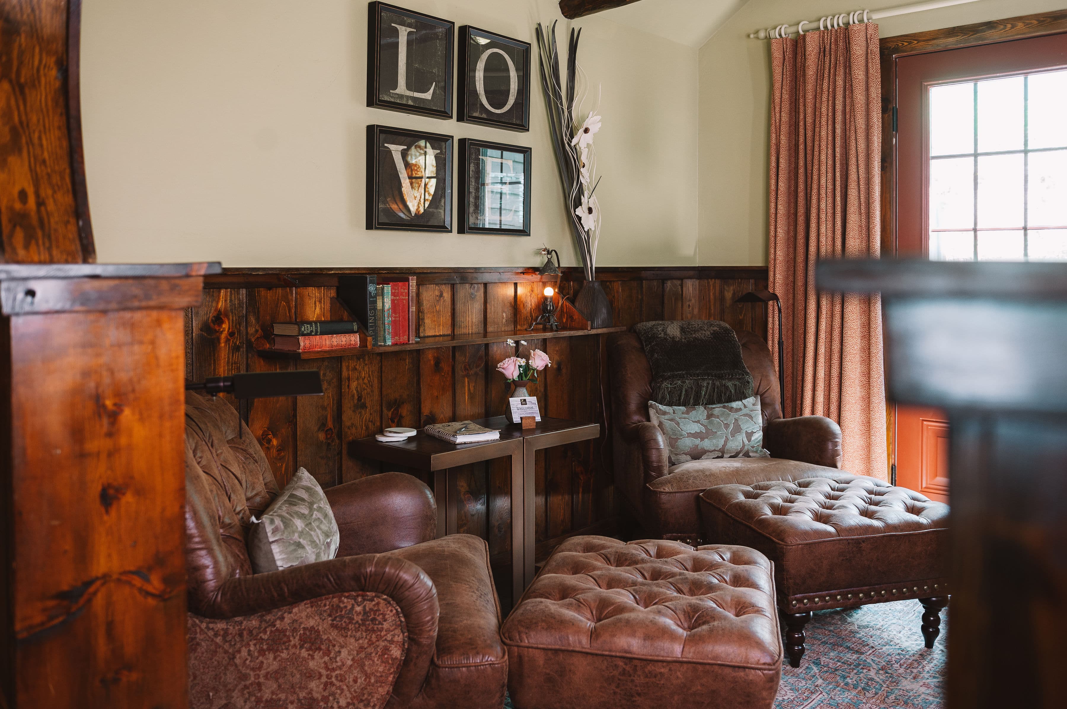A cozy sitting area featuring brown leather chairs, ottomans, bookshelves, and a warm atmosphere.
