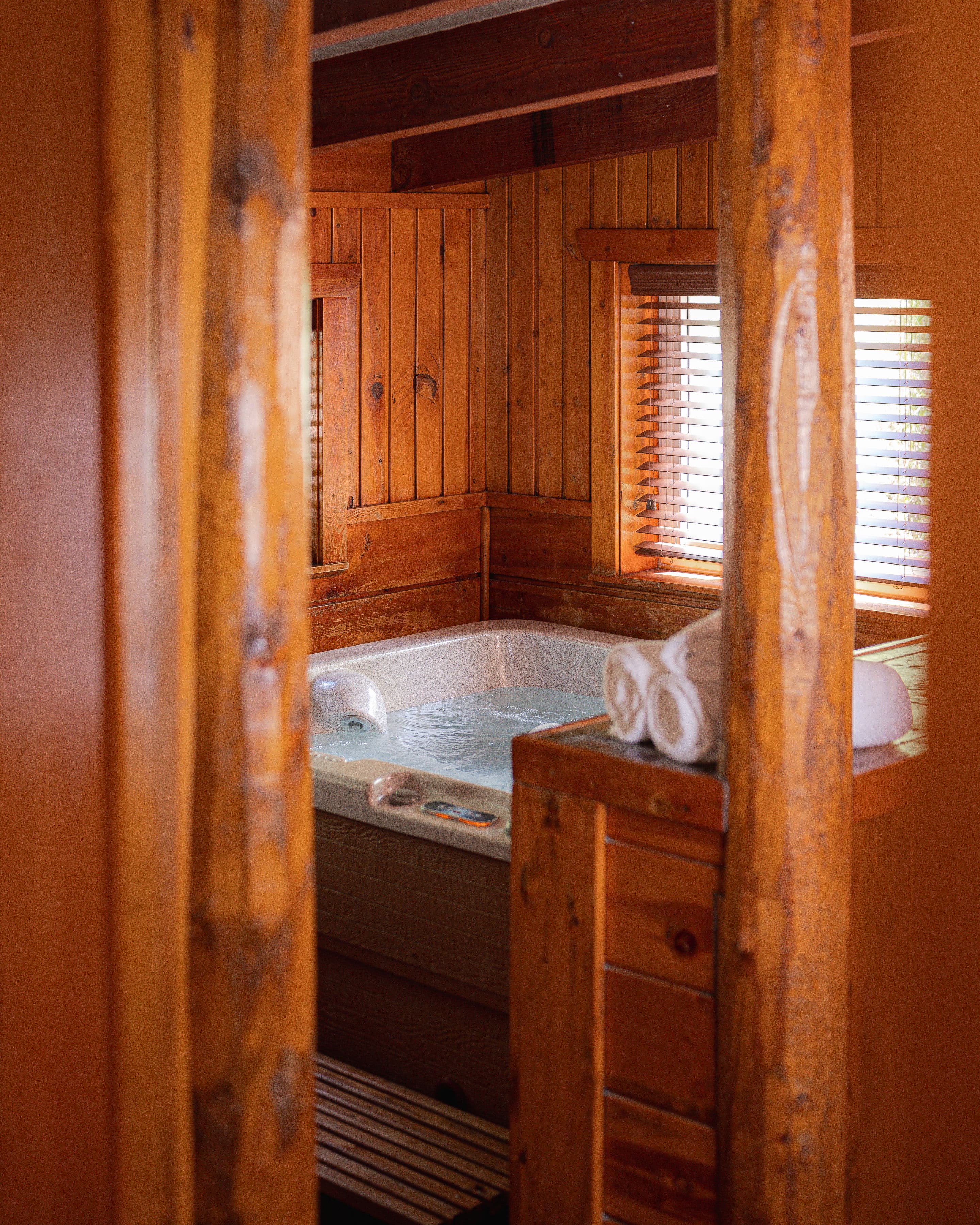 A cozy wooden room features a bubbling hot tub and neatly rolled towels.