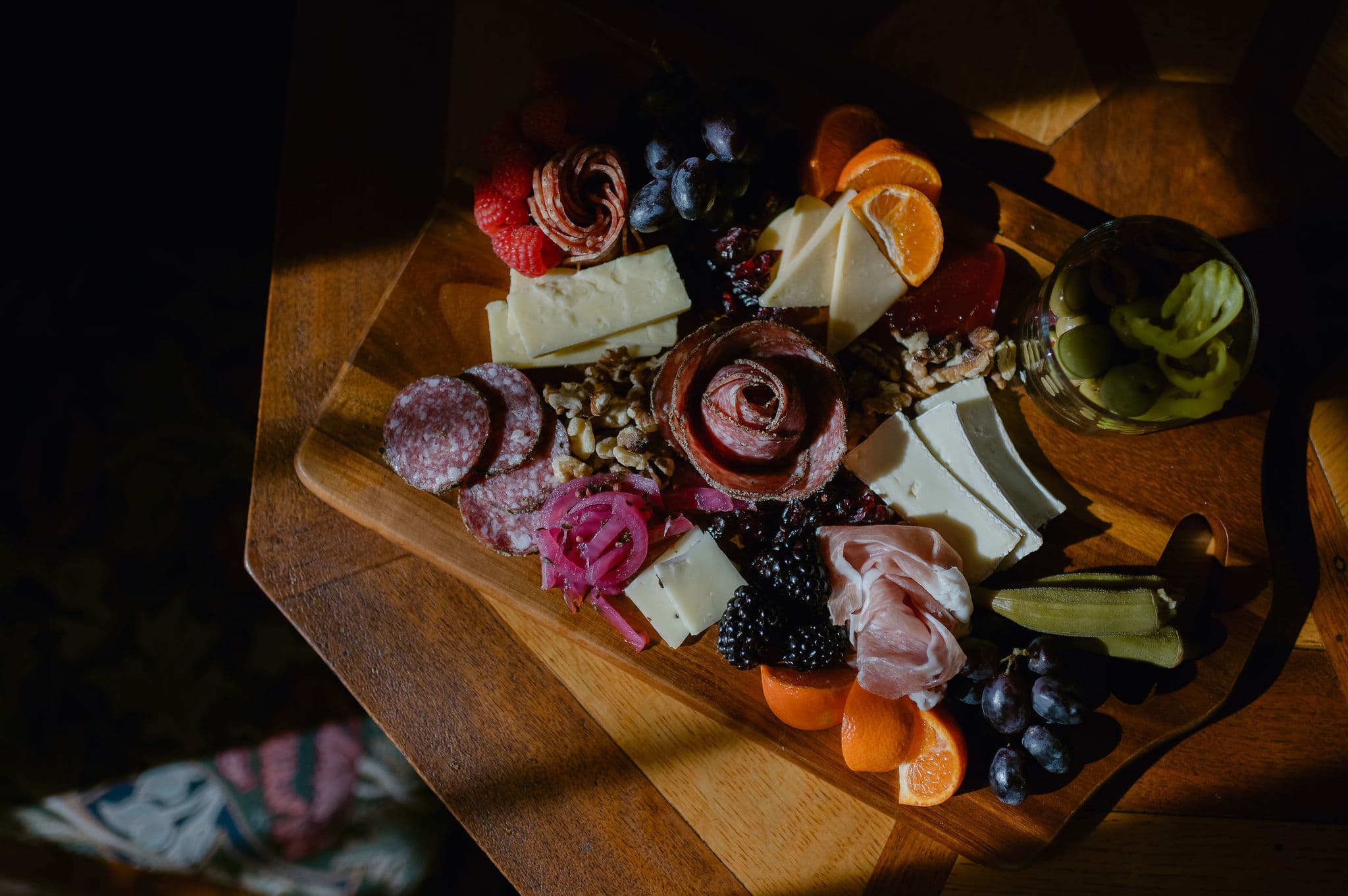 A wooden platter featuring an assortment of cured meats, cheeses, fruits, nuts, and pickles.