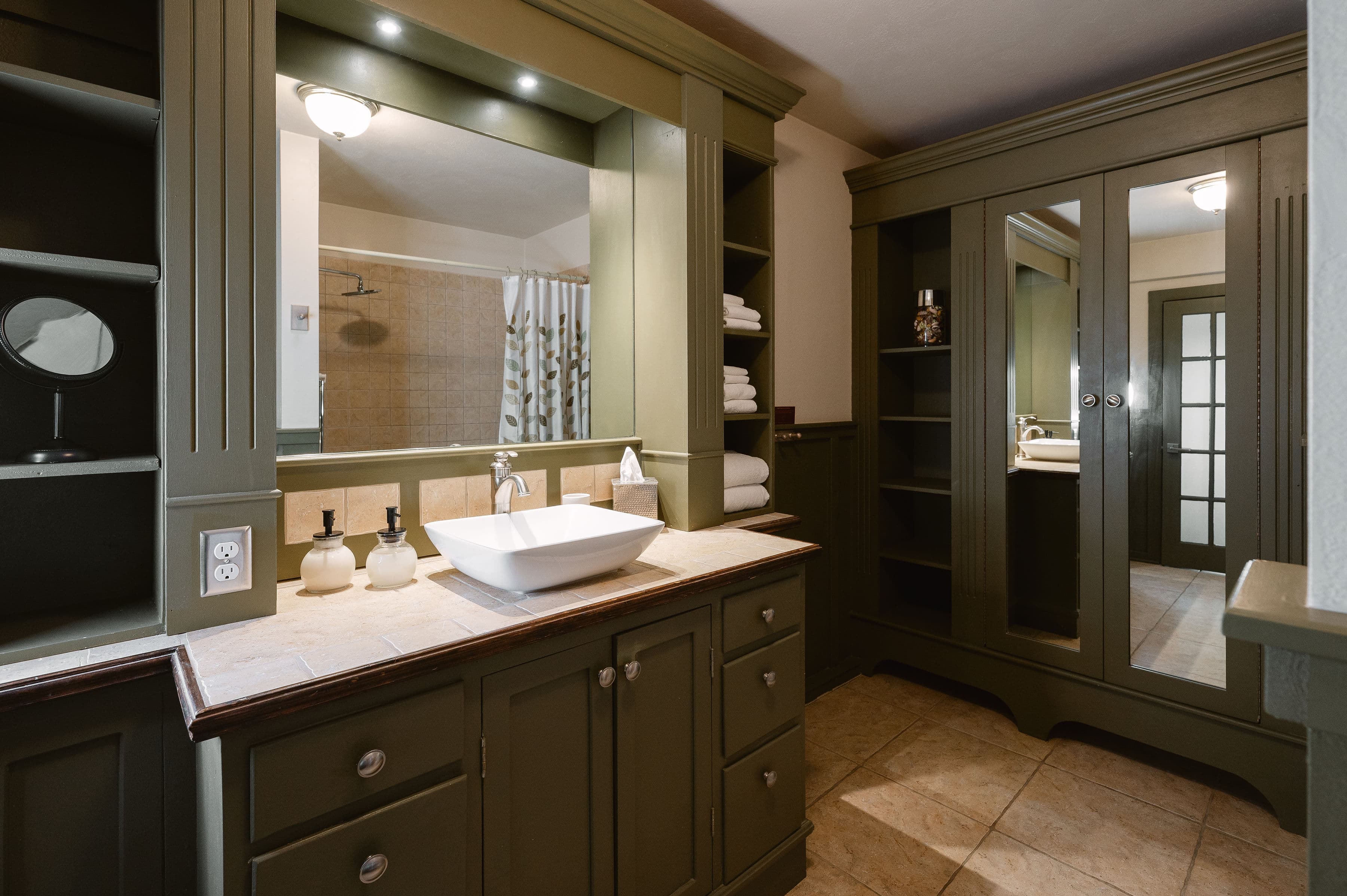 A stylish bathroom featuring green cabinetry, a modern sink, and neatly arranged towels.