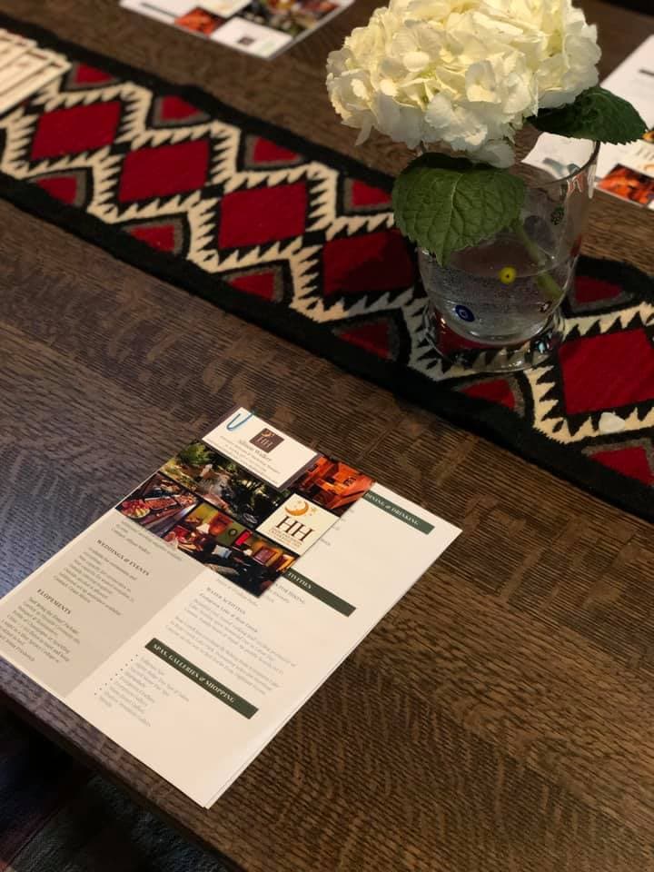 A dining table featuring a menu and a vase of white flowers on a patterned table runner.