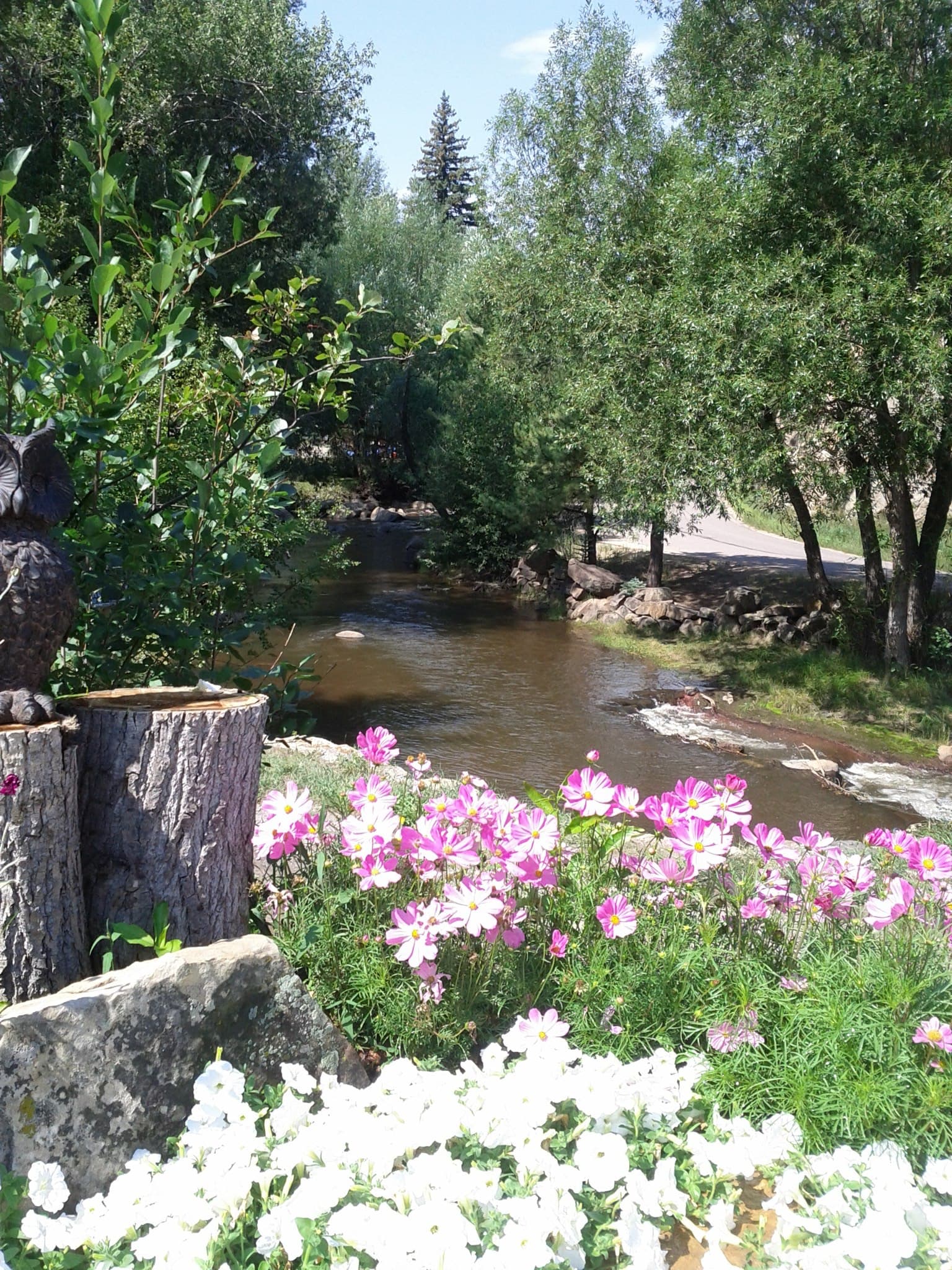 A serene river flows through a lush landscape adorned with colorful flowers and greenery.