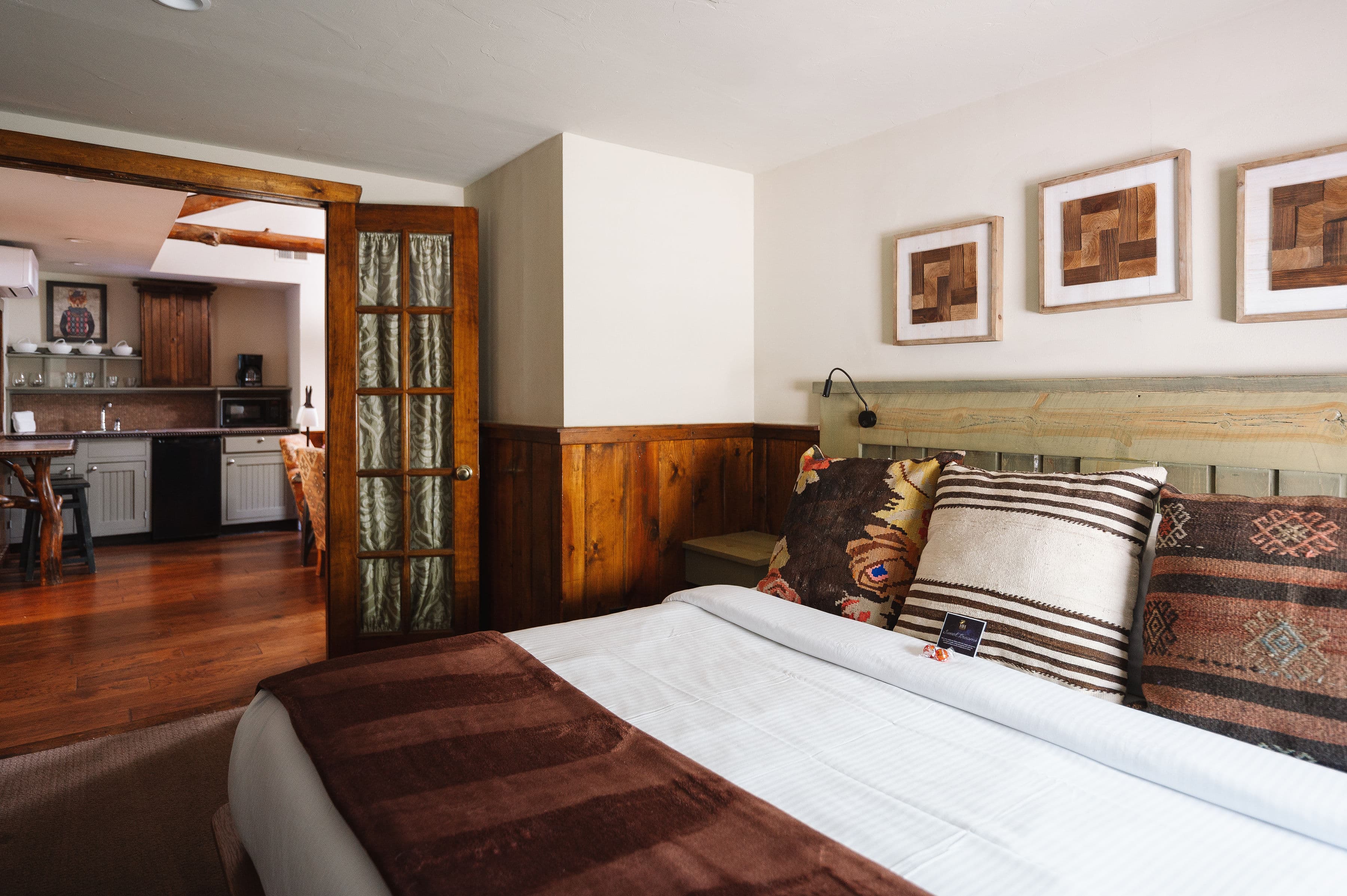 A cozy bedroom featuring a wooden bed, decorative pillows, and a view of an adjacent kitchen area.