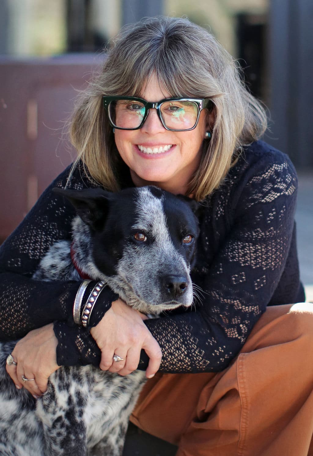 A smiling woman with glasses embraces her black and white dog.