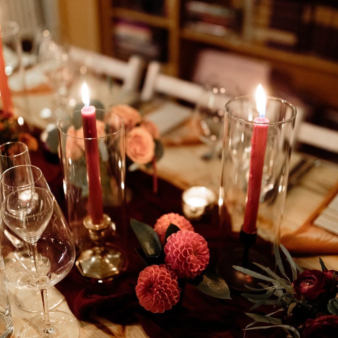 A beautifully set dining table adorned with red candles, floral arrangements, and elegant glassware.