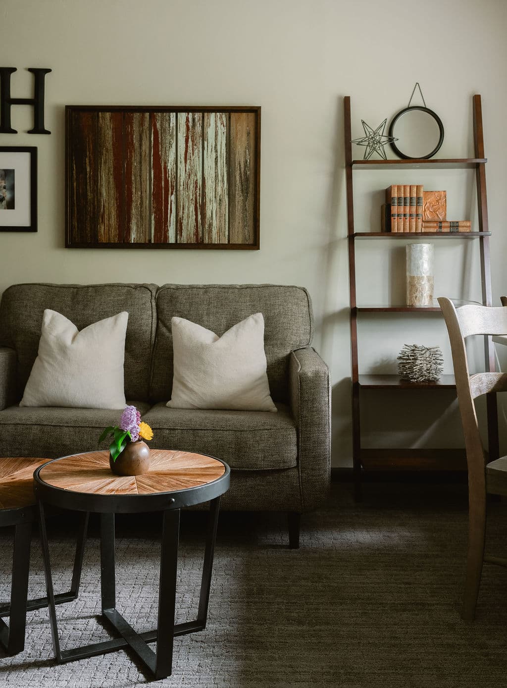 A cozy living room featuring a gray couch with decorative pillows, two round wooden tables, and a stylish bookshelf.