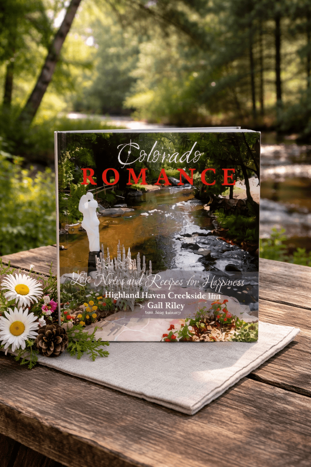 A book titled "Colorado Romance" featuring a tranquil creek scene, placed on a rustic wooden table adorned with flowers and pinecones.
