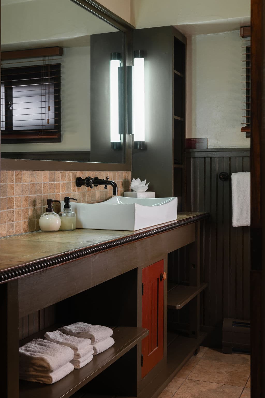 A modern bathroom with a stylish sink, toiletries, and neatly folded towels on a wooden shelf.