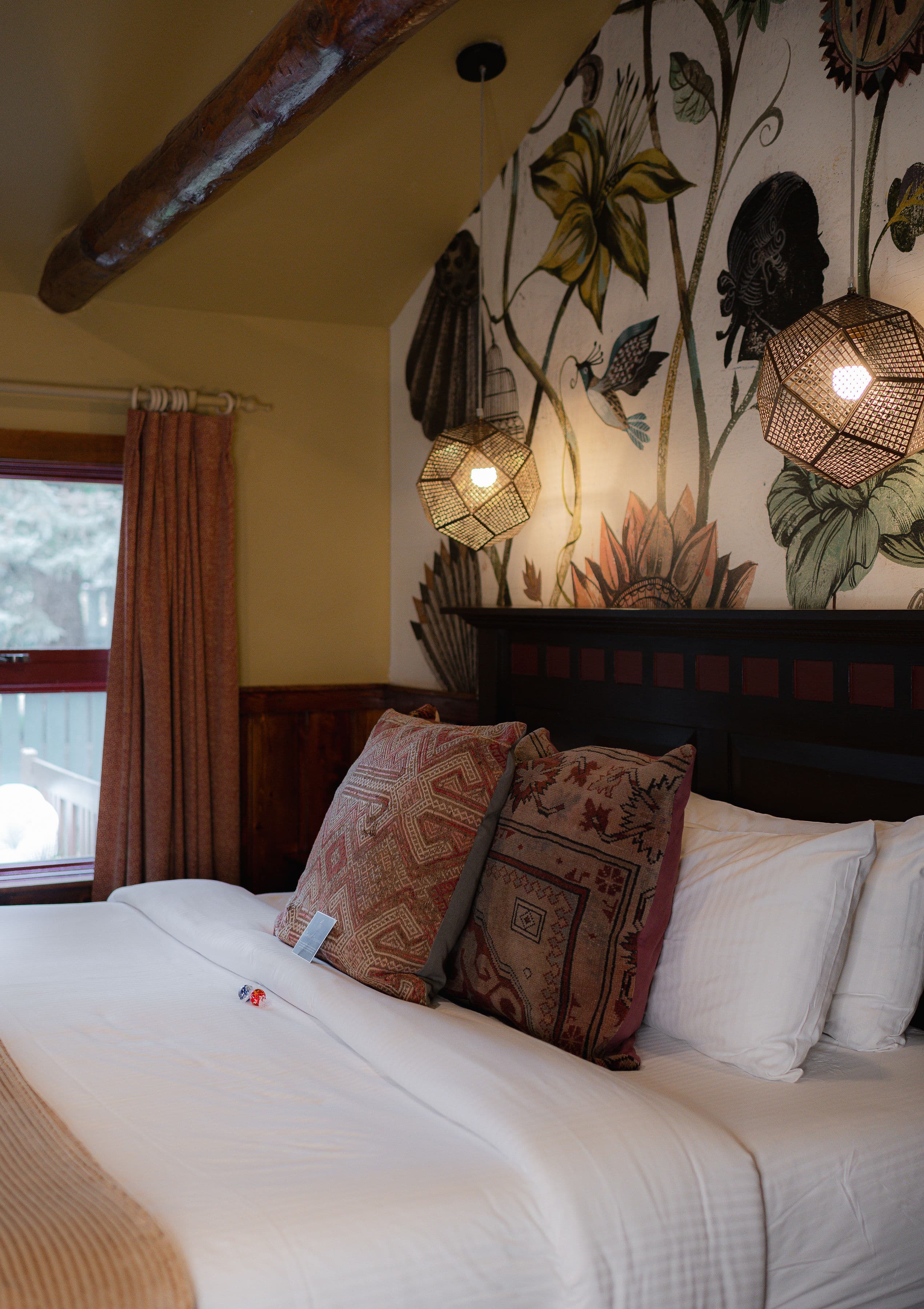 A cozy bedroom featuring a bed with decorative pillows, a floral wall mural, and pendant lights.
