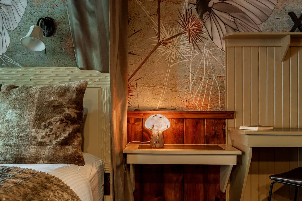 A cozy bedroom corner featuring a patterned pillow, a decorative lamp, and a mural of butterflies on the wall.