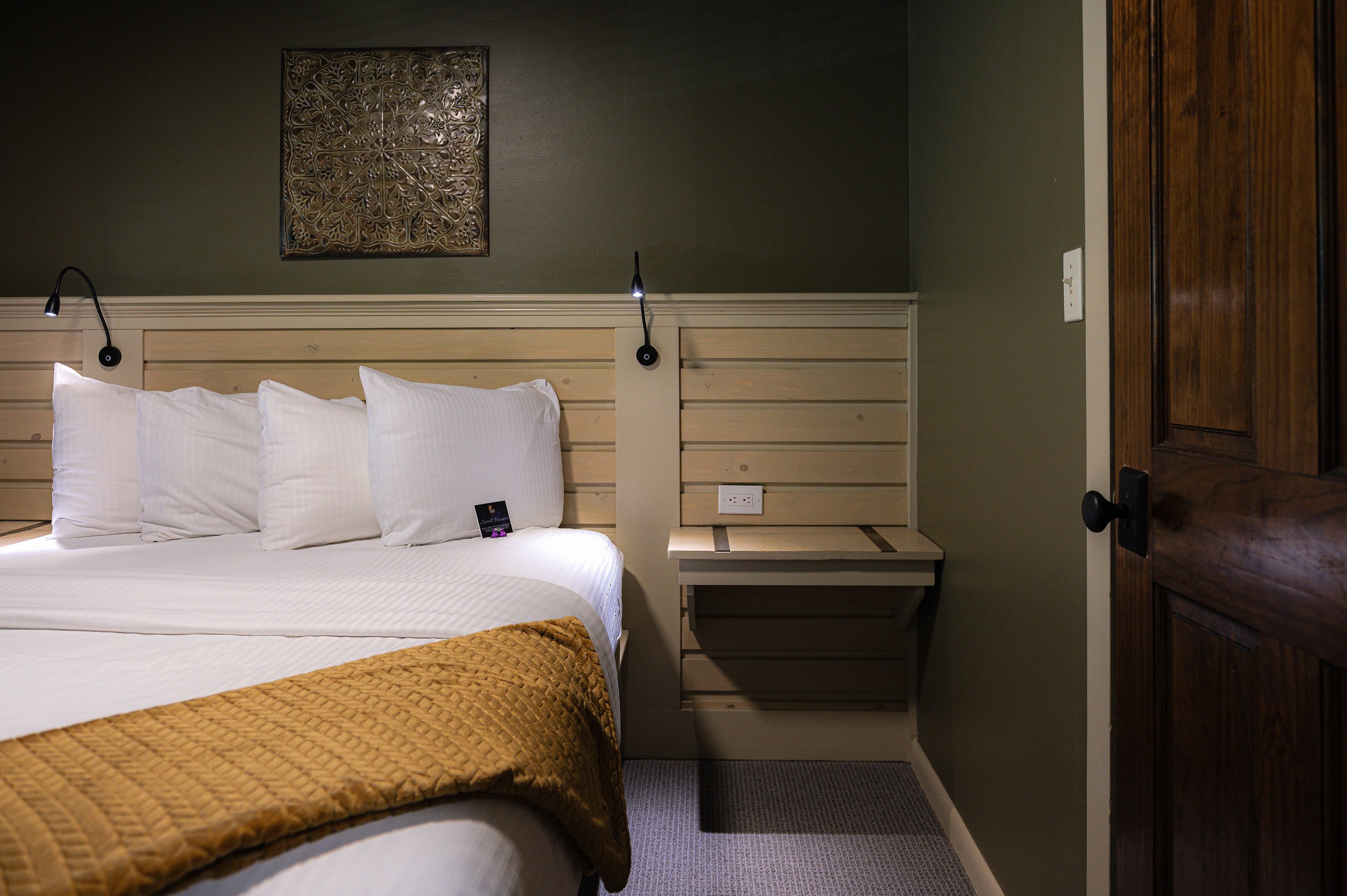 Cozy bedroom featuring a bed with white pillows, a golden throw, and a small desk against a green wall.