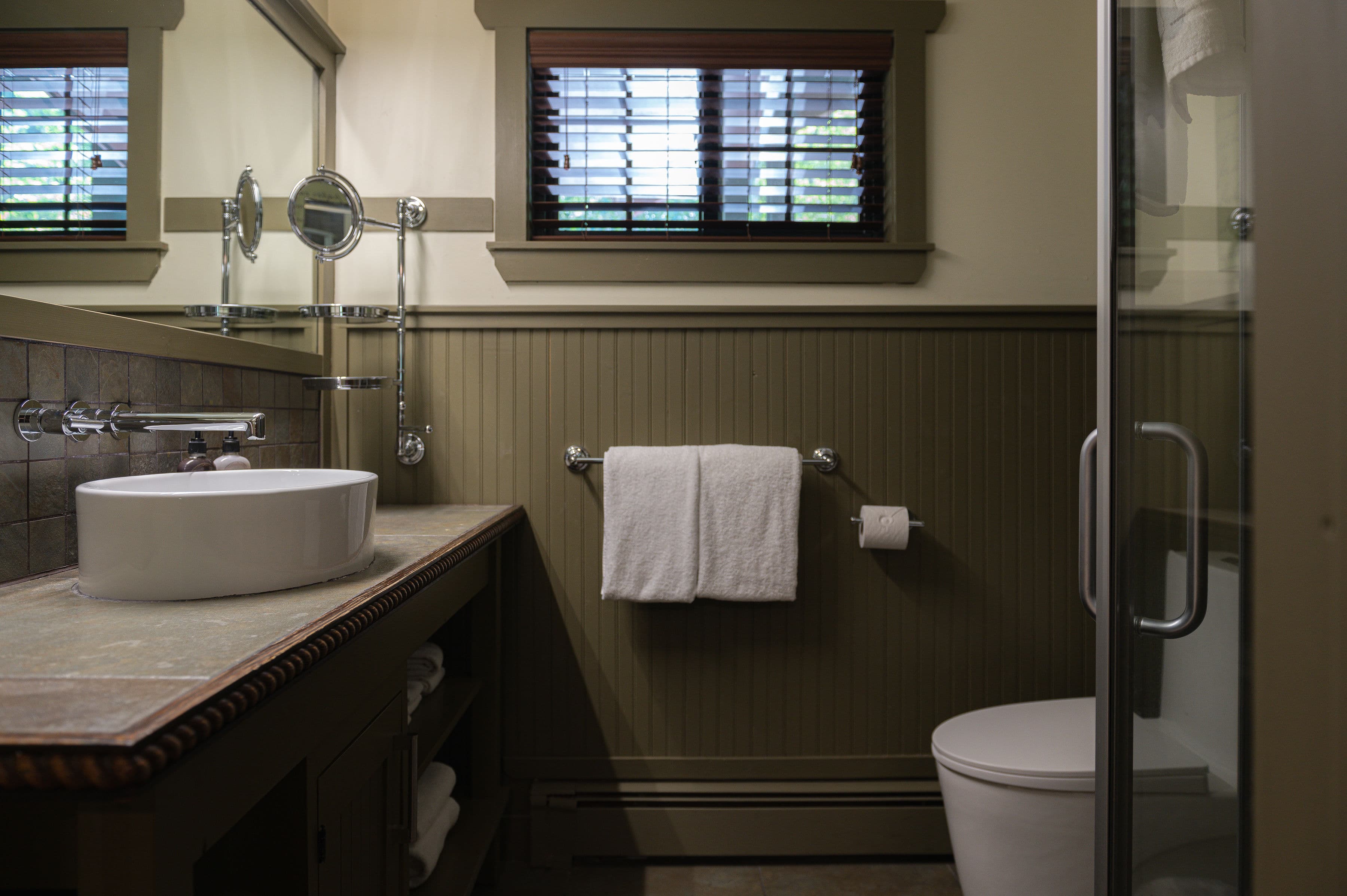 A modern bathroom with a white sink, towels, and a glass shower.