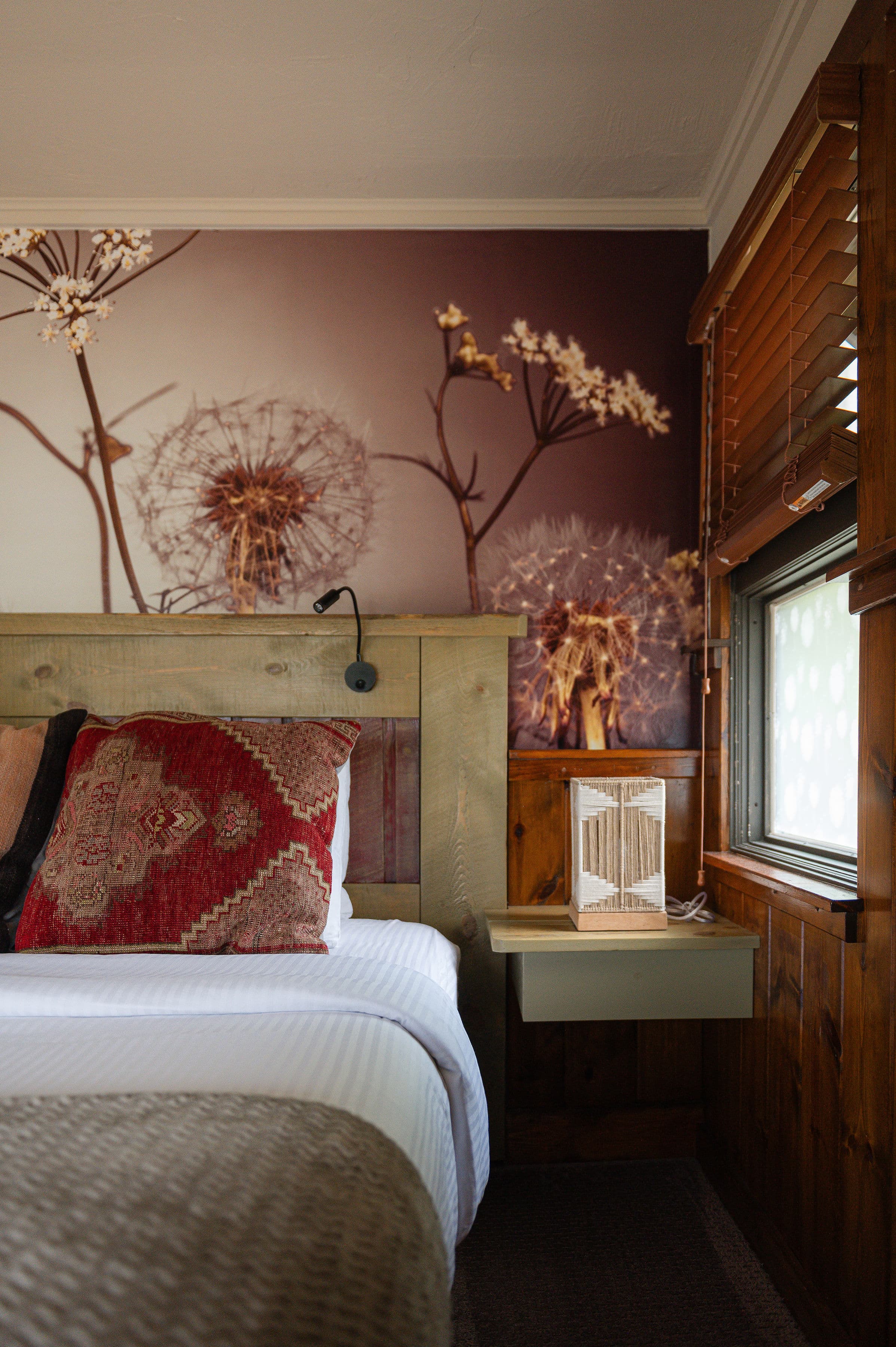 king bed with soft bedding, graphic dandelion wallpaper above bed and wood paneling