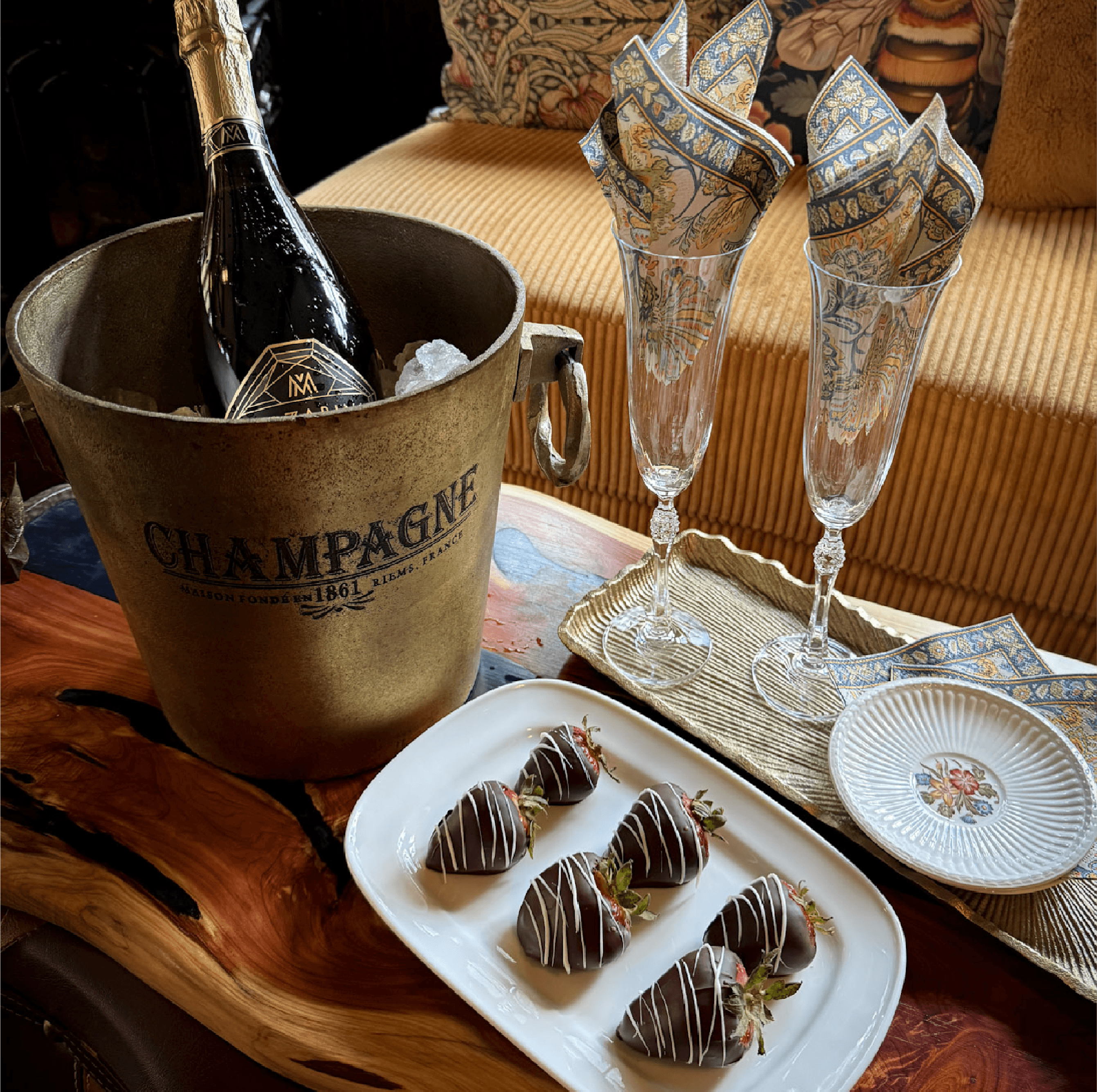 A chilled champagne bottle in a bucket alongside chocolate-covered strawberries and elegant glasses.