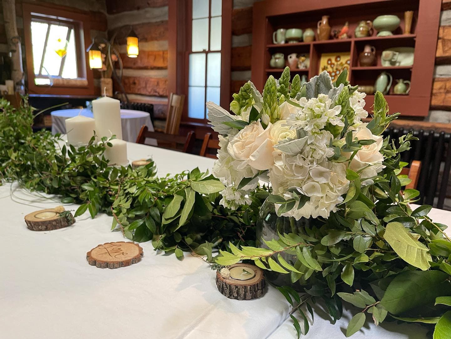 A beautifully arranged table centerpiece featuring a floral bouquet surrounded by greenery and candles.