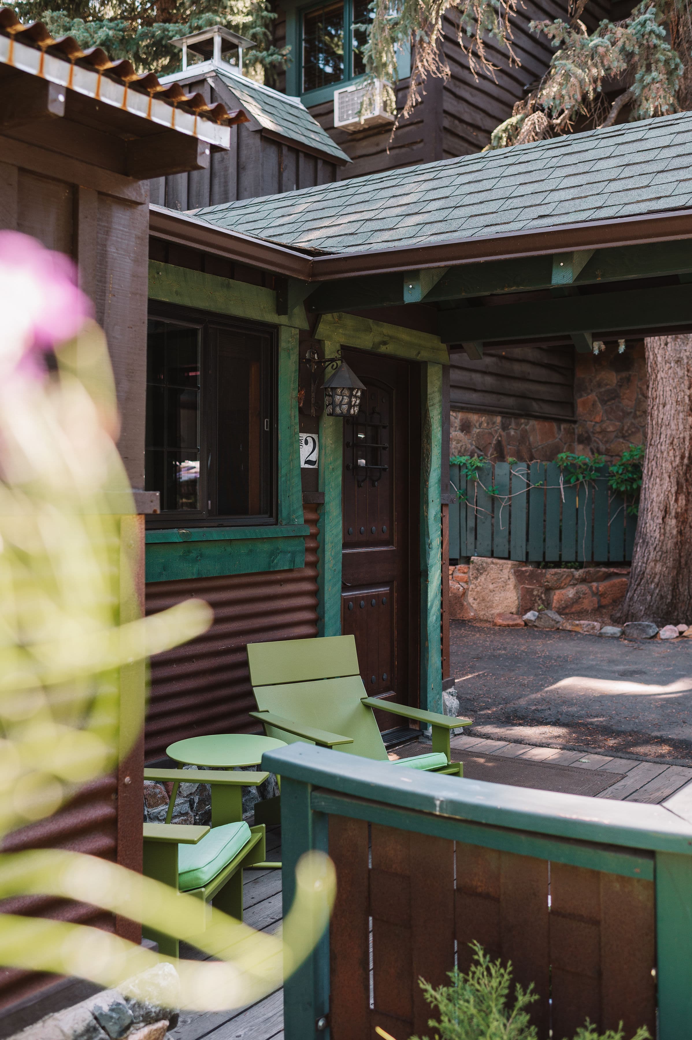 A charming entrance with a wooden door, green accents, and two green chairs beside a rustic cabin.