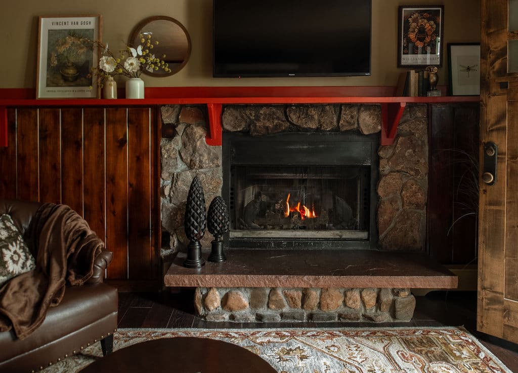 Cozy living room featuring a stone fireplace with a fire, a dark leather chair, and a mounted TV.