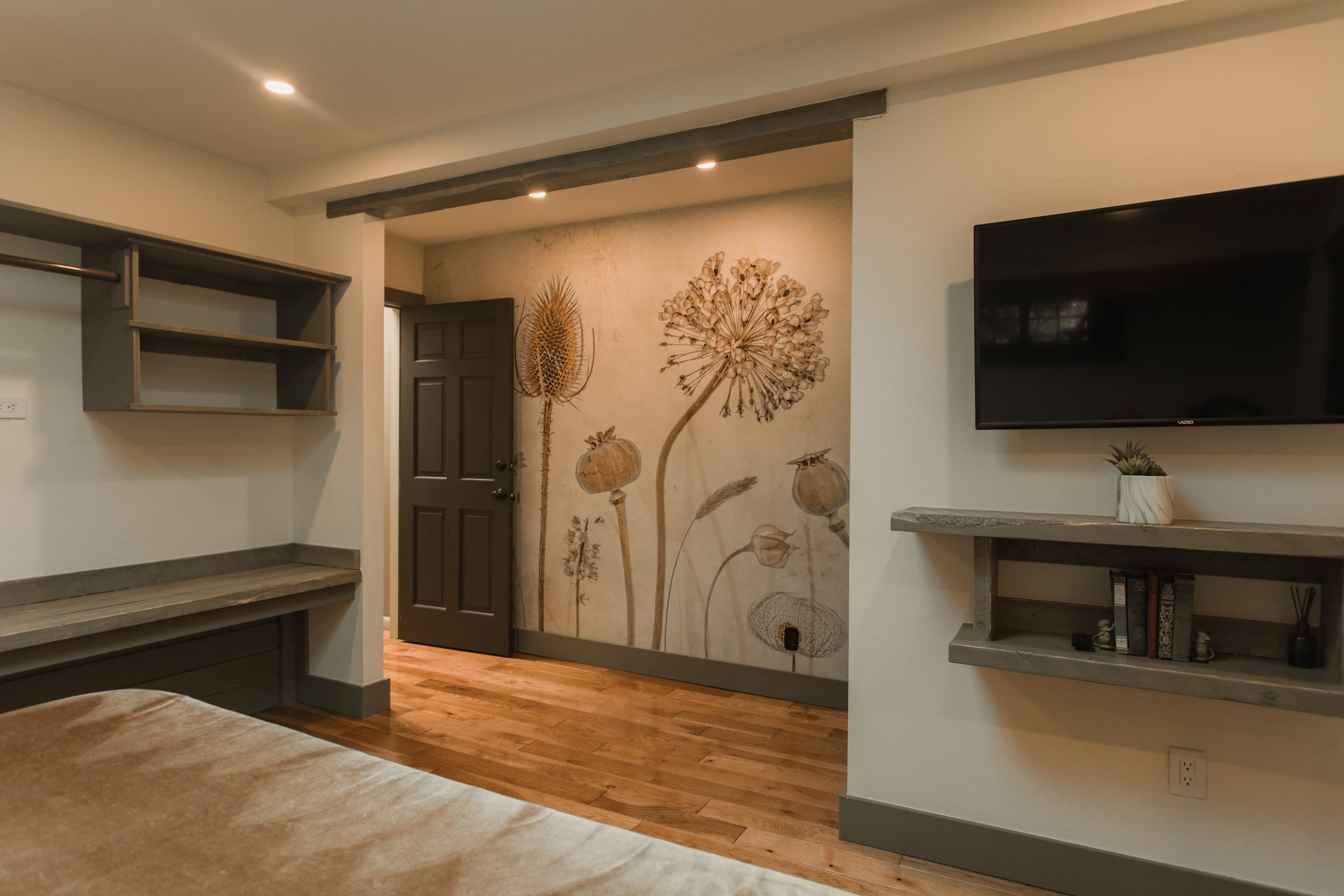 A cozy room featuring a floral mural, dark door, TV, and wooden shelving.
